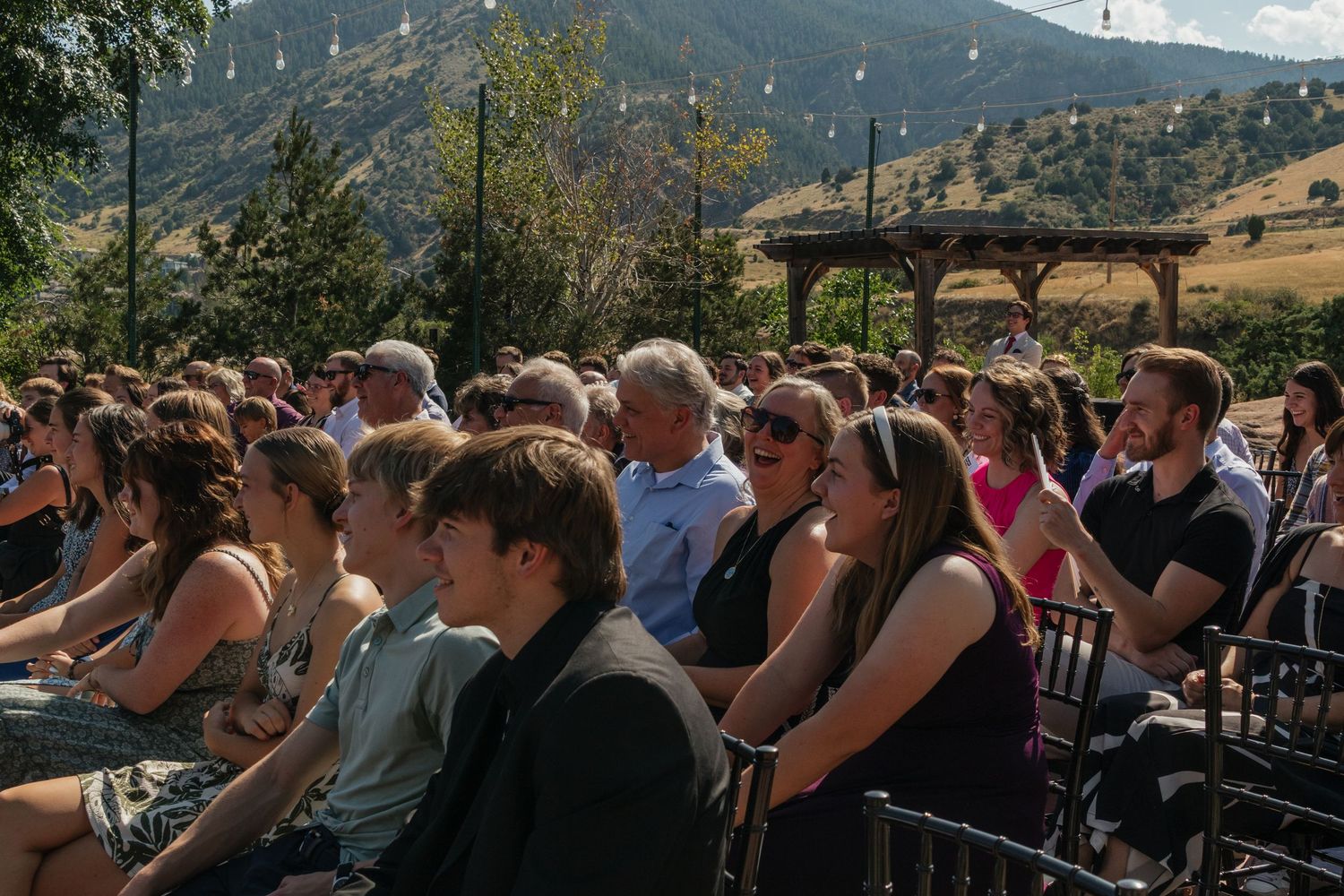 Wedding guests seated outdoors at a scenic mountain venue during a ceremony.