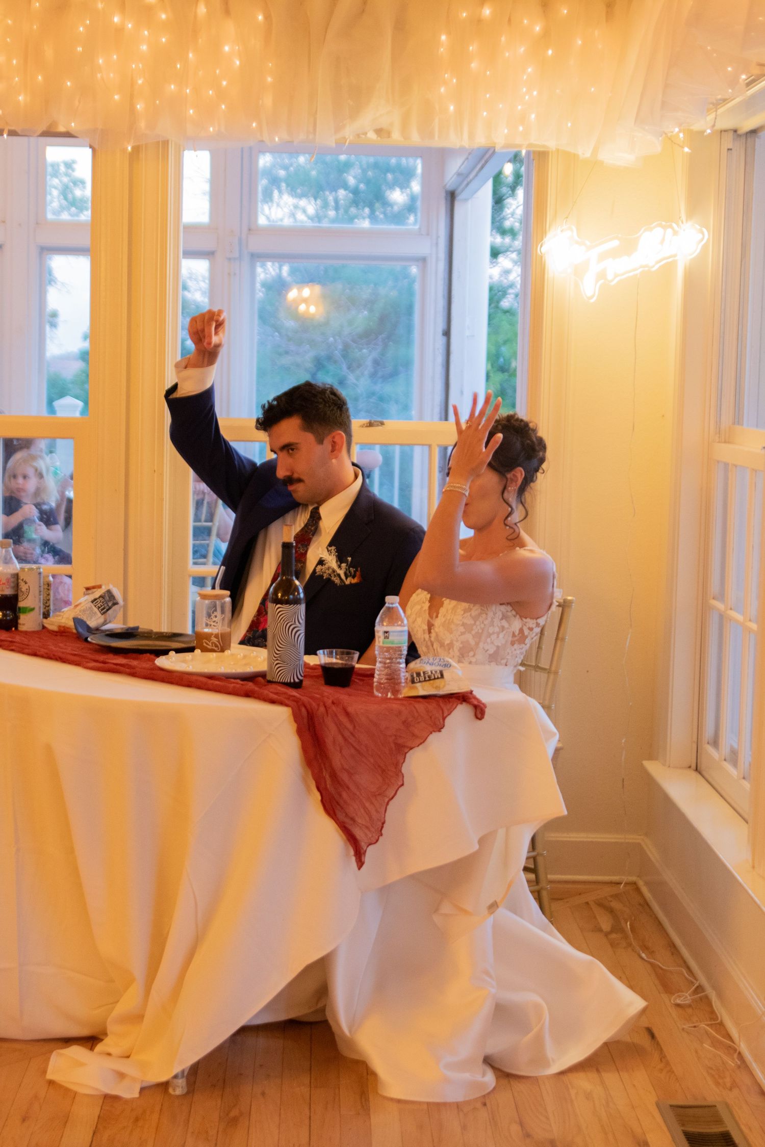 Wedding couple at reception table under glowing string lights.