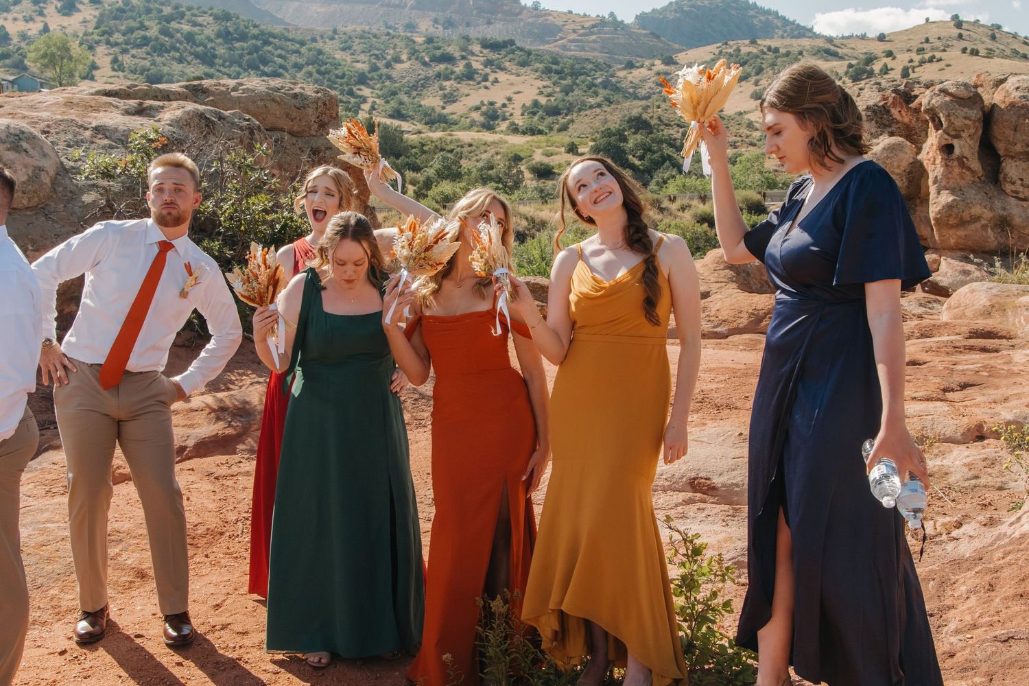 Wedding party in burgundy and green dresses celebrating against desert mountain backdrop.
