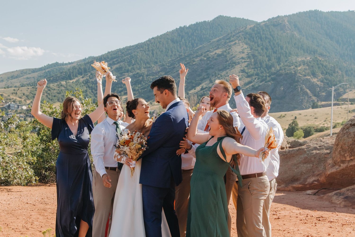 Wedding celebration with group dancing and embracing on scenic mountain terrain.