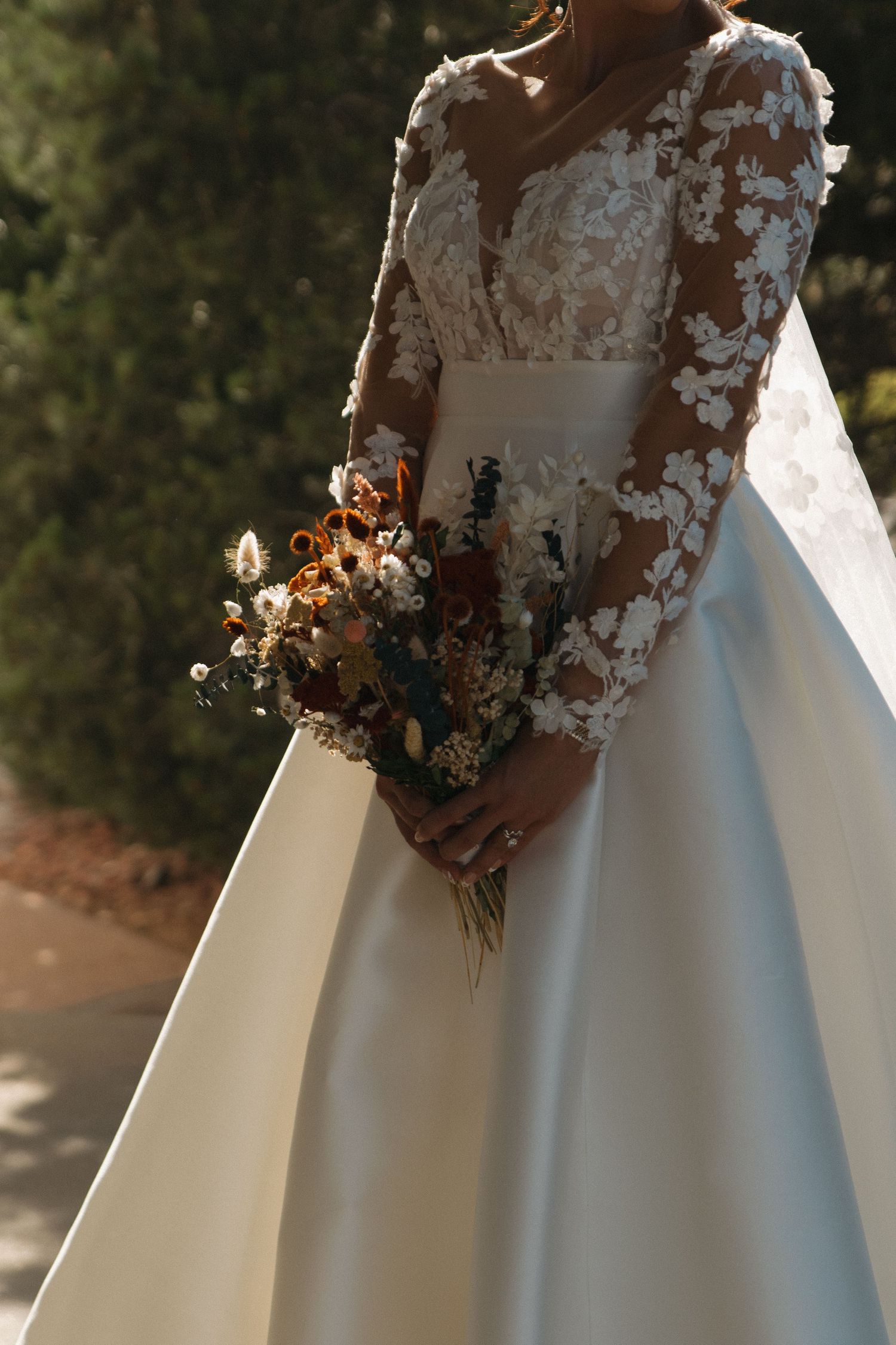 Detail shot of wedding dress with intricate lace sleeves and floral bouquet.