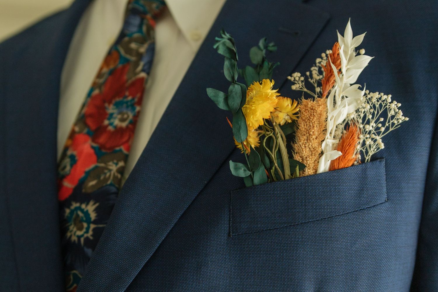 Close-up details of colorful floral pocket square in navy suit jacket.