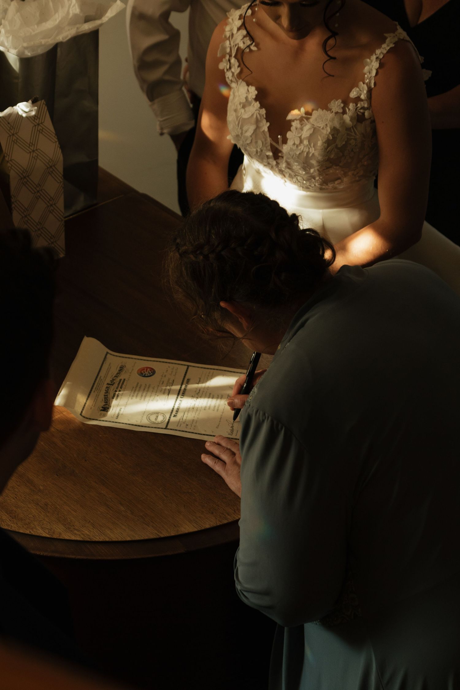 Close-up shot of wedding paperwork being signed on dark wooden surface in dramatic lighting.