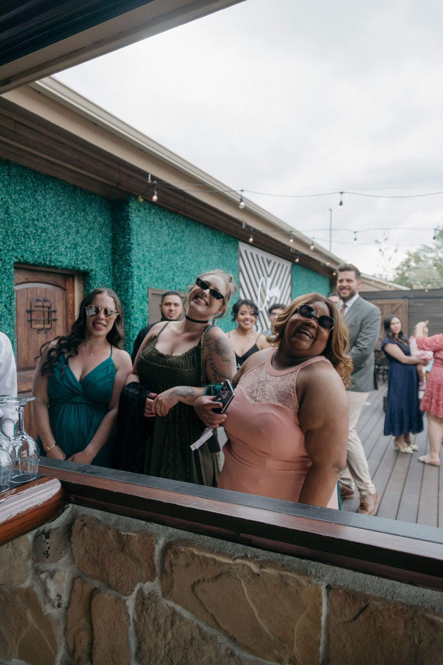 Wedding guests posing and smiling at an outdoor bar during a wedding reception.