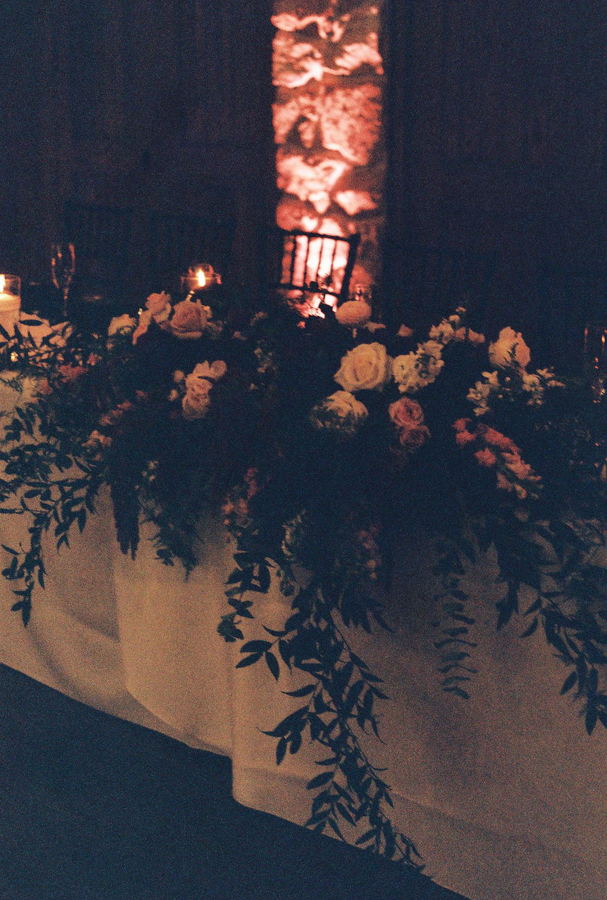 Romantic candlelit wedding sweetheart table with lush floral arrangement at night.