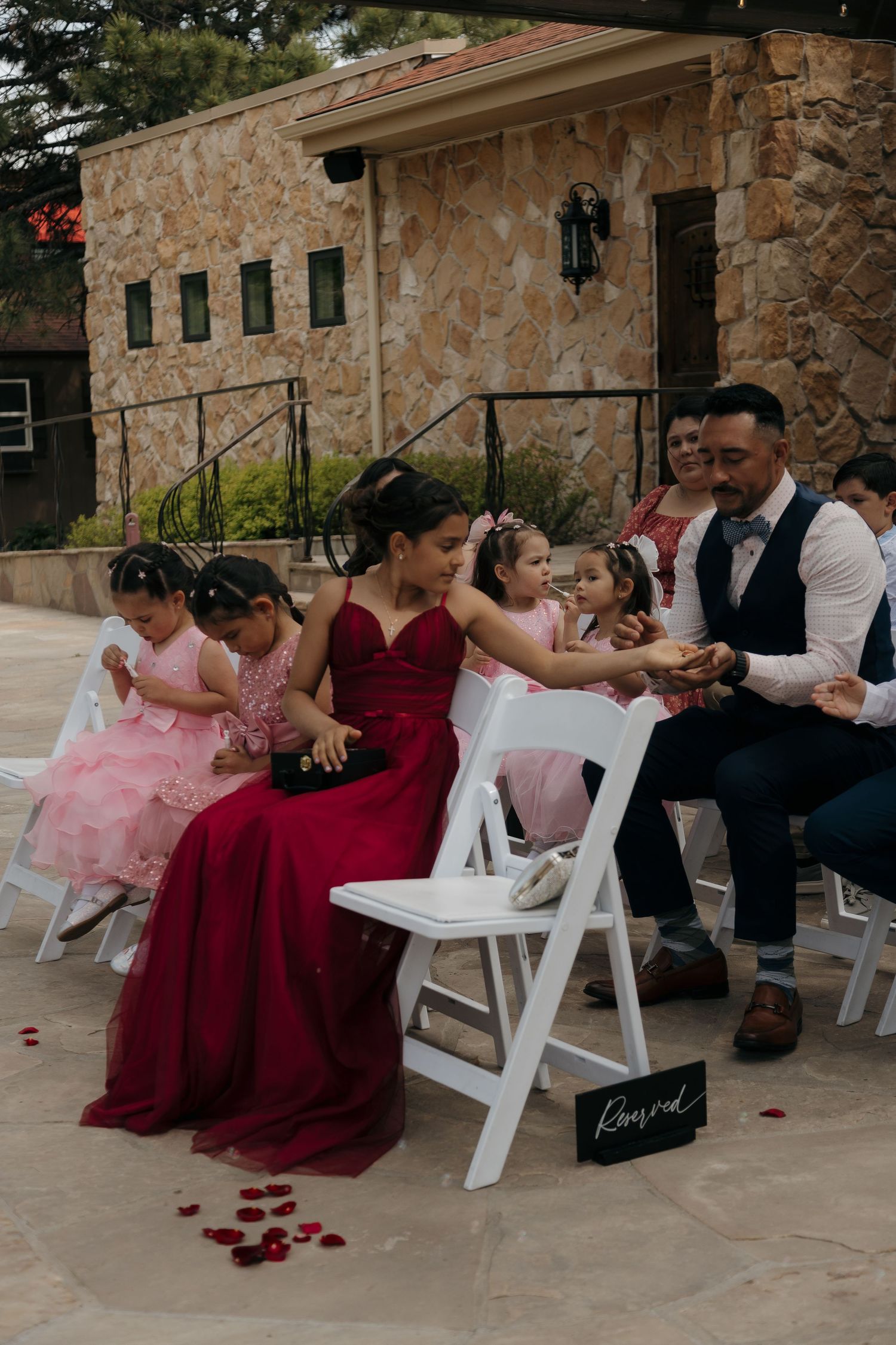 Wedding guests in red and pink formal dresses seated at outdoor ceremony reserved section.