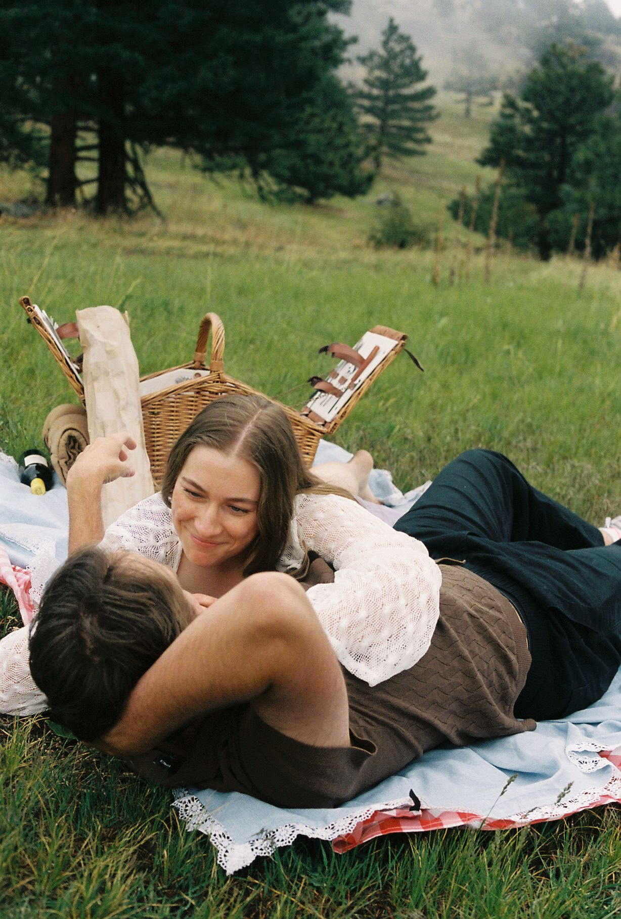 Romantic couple relaxing on picnic blanket in green meadow with wicker basket.