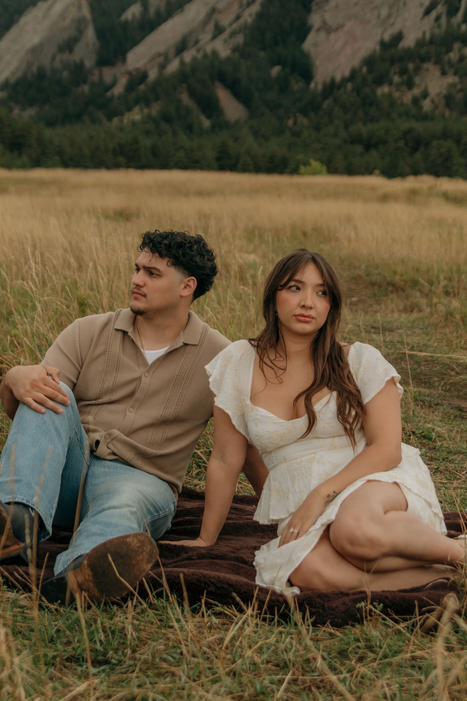 Couple sitting on blanket in grassy field with rocky mountain flatirons backdrop.
