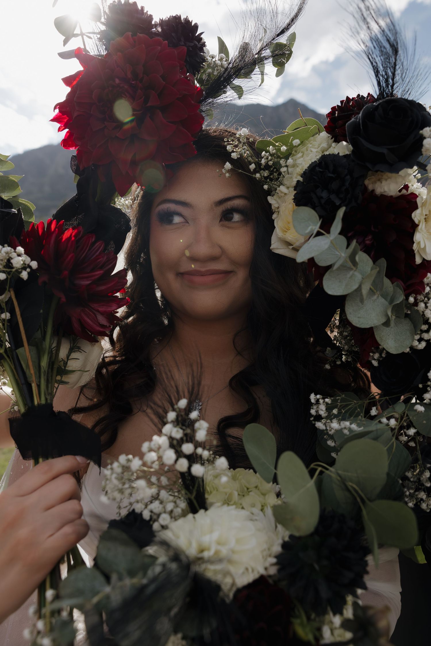 Bride surrounded by red, black, and white floral bouquets with mountain backdrop.