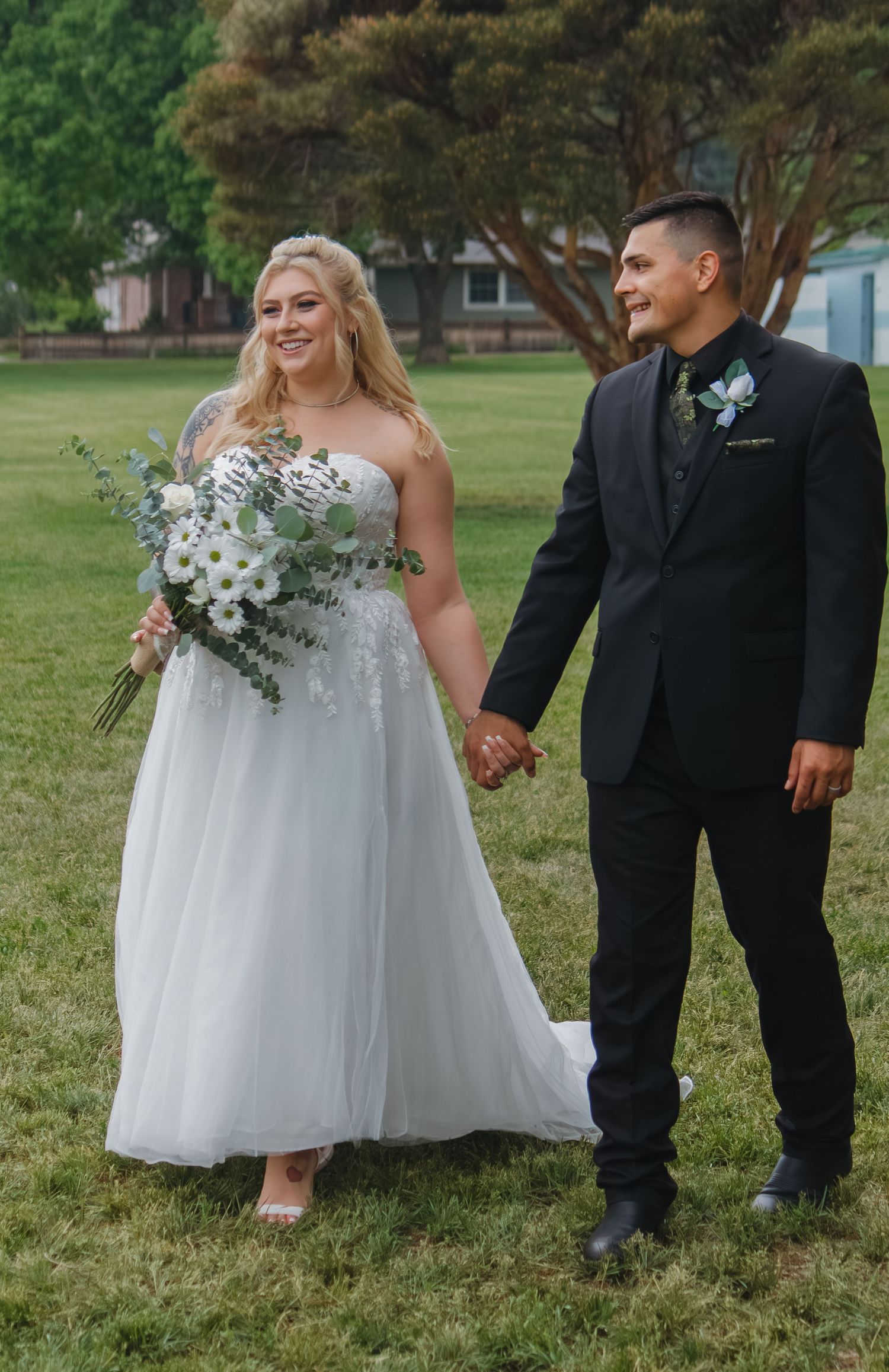 Formal wedding attire and floral bouquet details captured on green lawn.