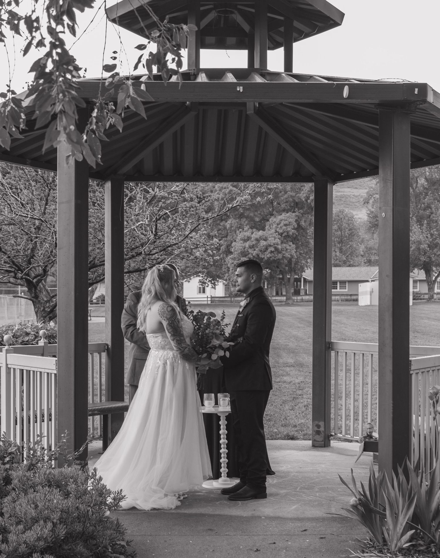 A couple stands face to face during their wedding ceremony in a park gazebo.