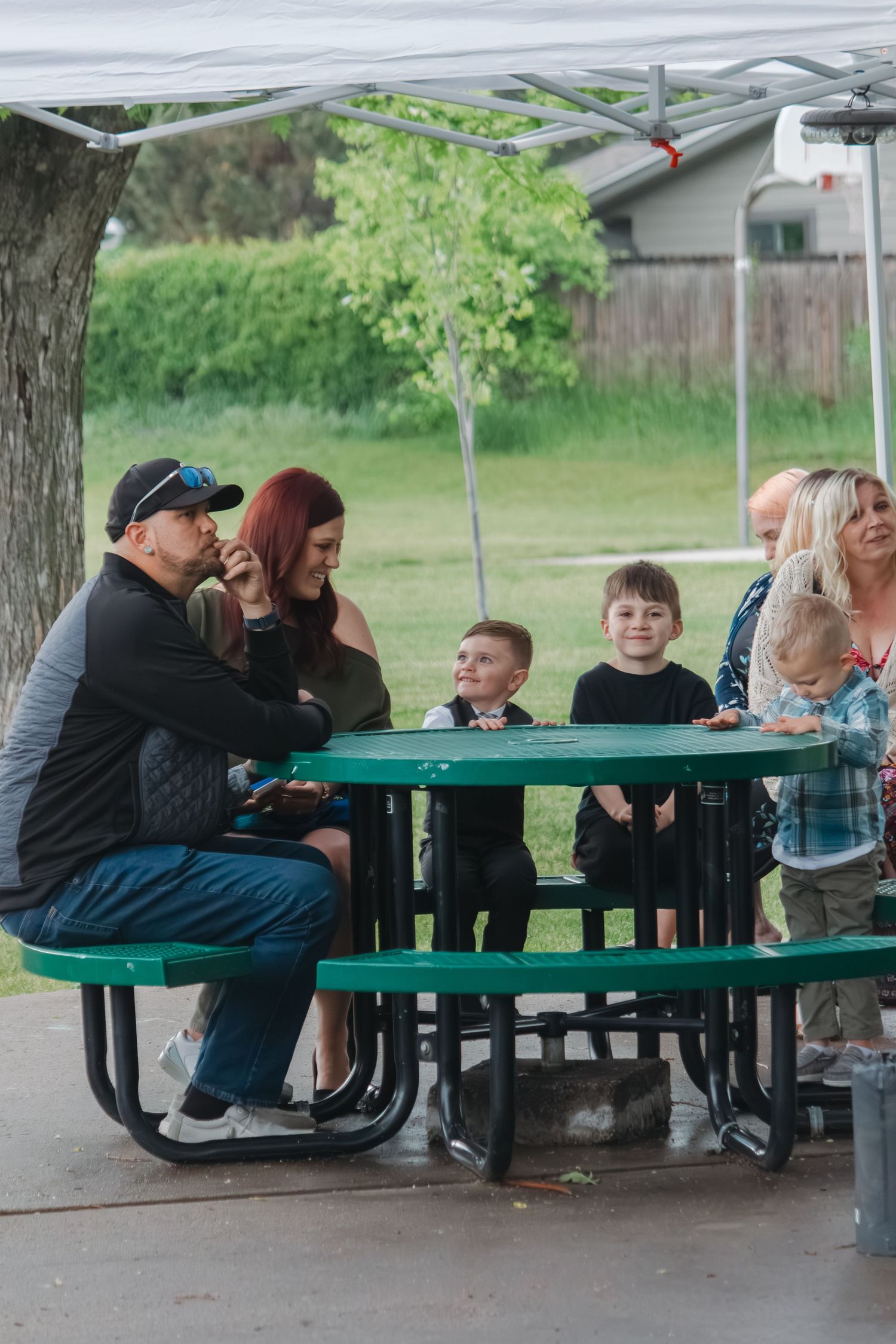 Wedding guests gather at a picnic table under a covered outdoor area.