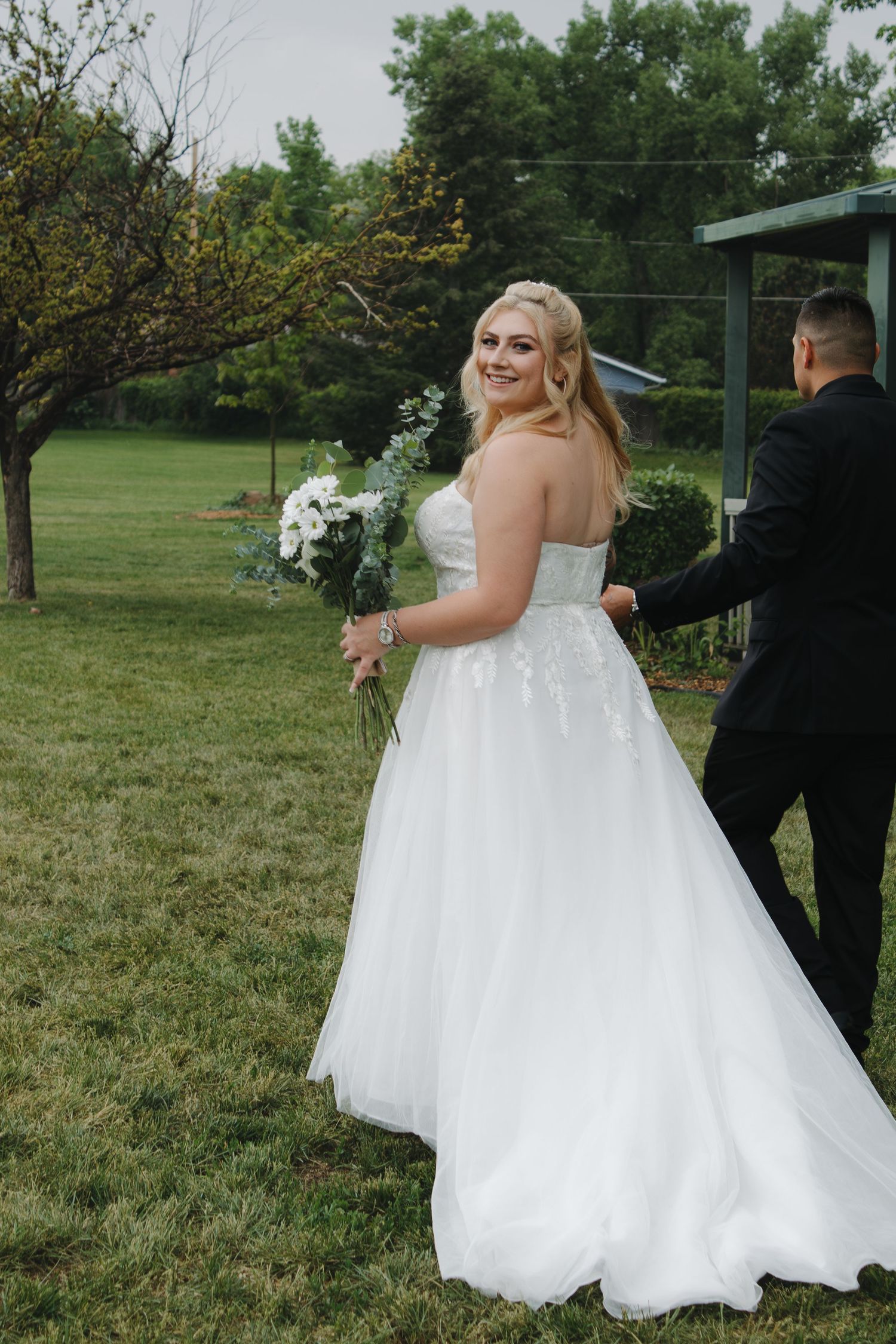 A bride in a flowing white gown holds a bouquet while posing in a garden setting.