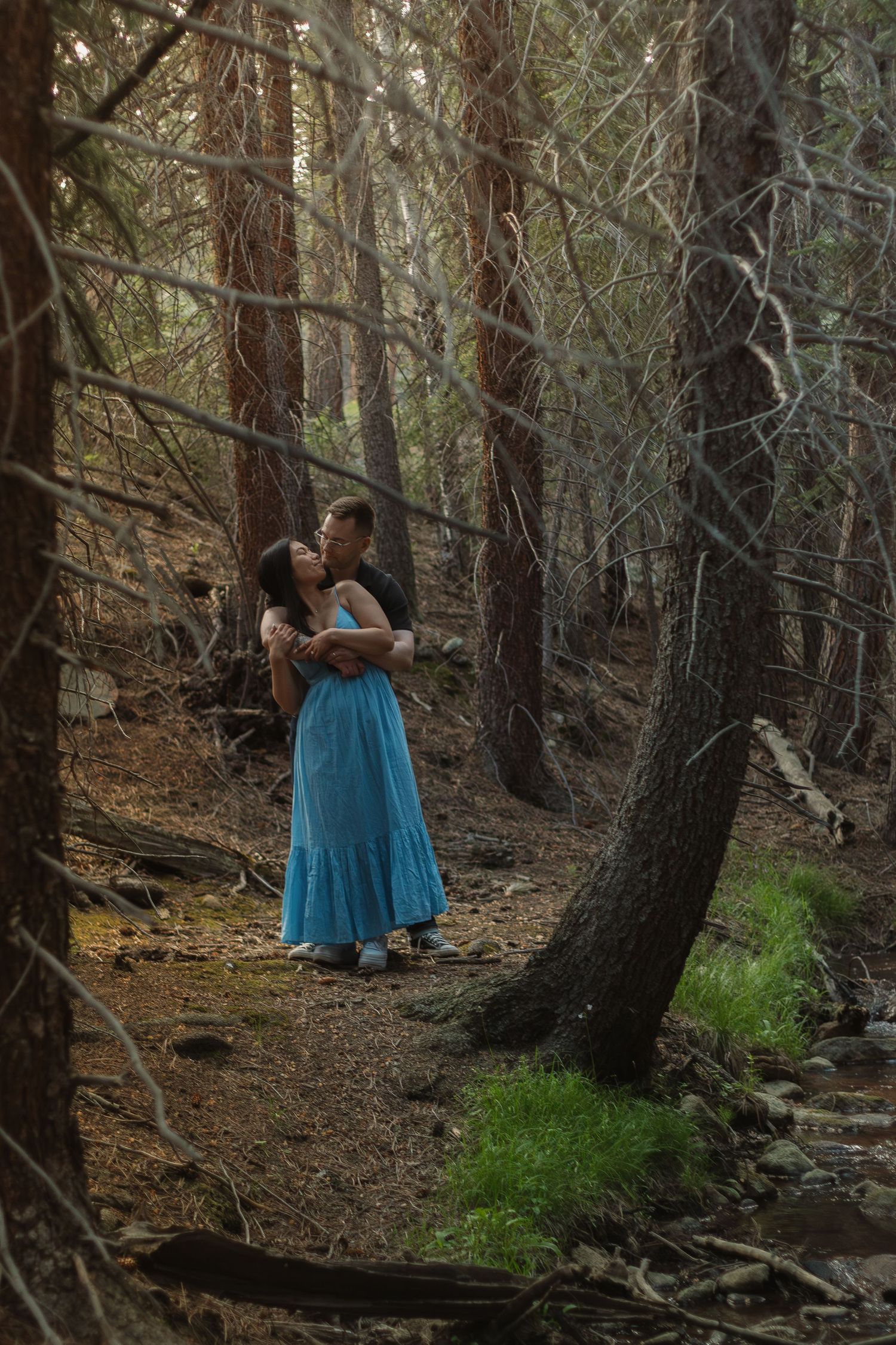 A couple shares an intimate moment on a forest path beside a small stream.