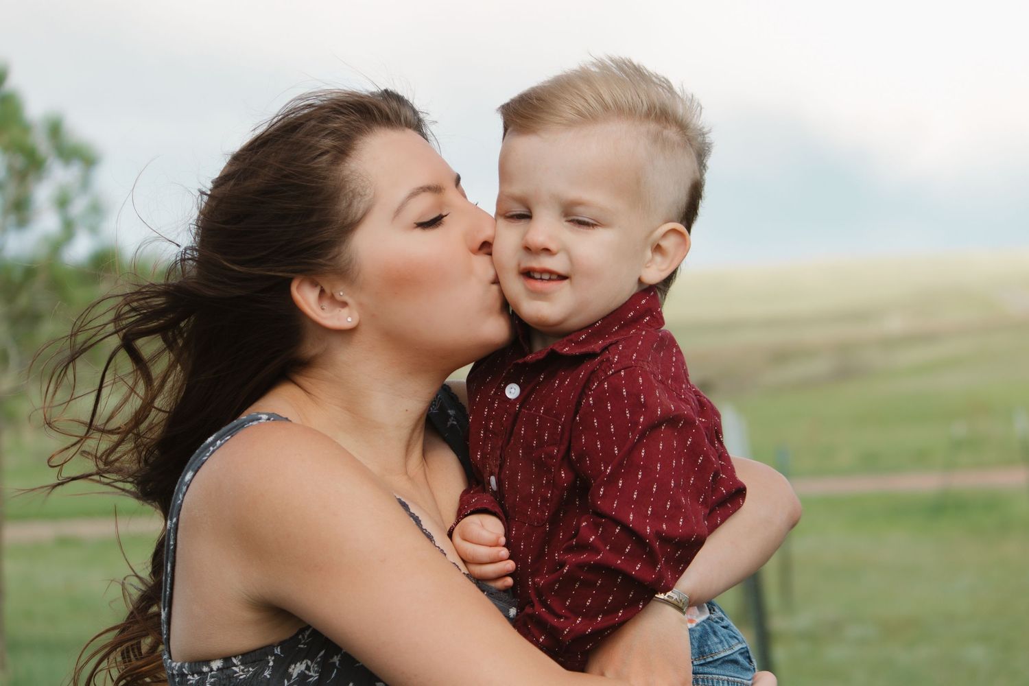 A tender family moment captured outdoors with a scenic countryside background.