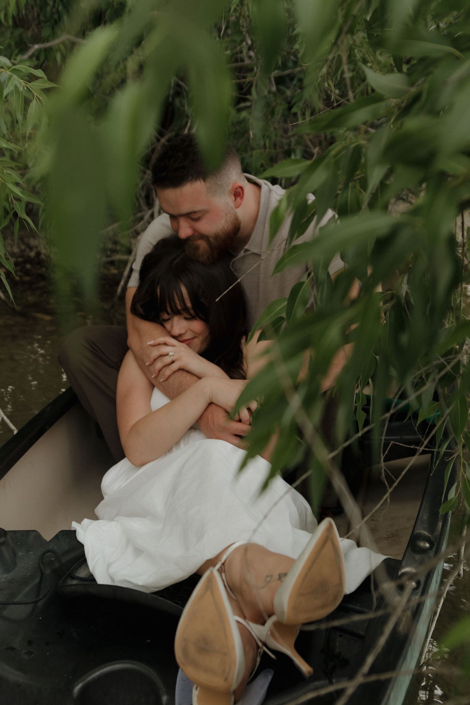 A couple sharing an intimate moment in a boat under overhanging green foliage.