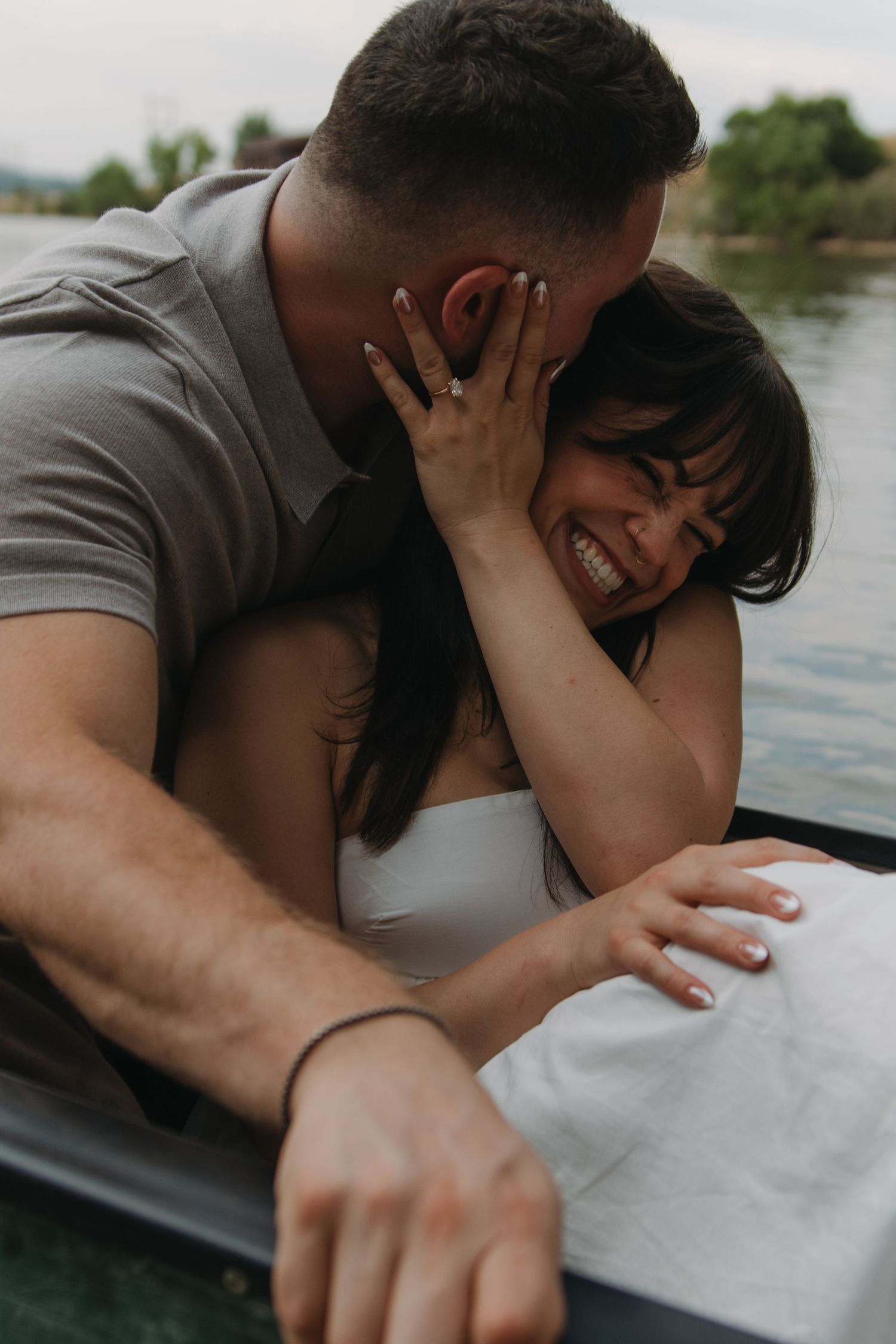 A romantic couple leans close together while sitting in a canoe on a tranquil lake.