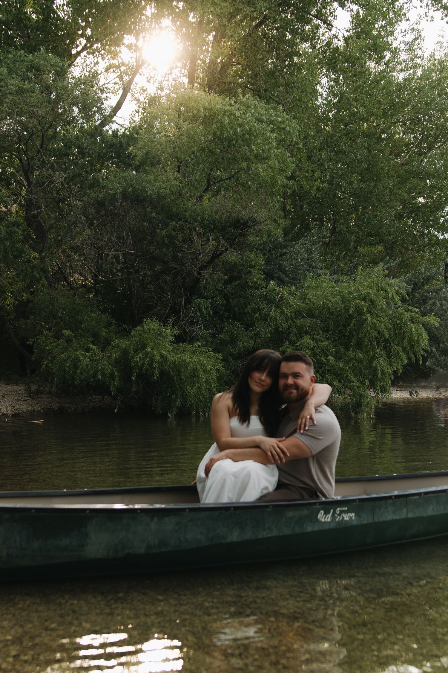 Romantic couple sharing an intimate moment in a green canoe on a tranquil lake during golden hour.