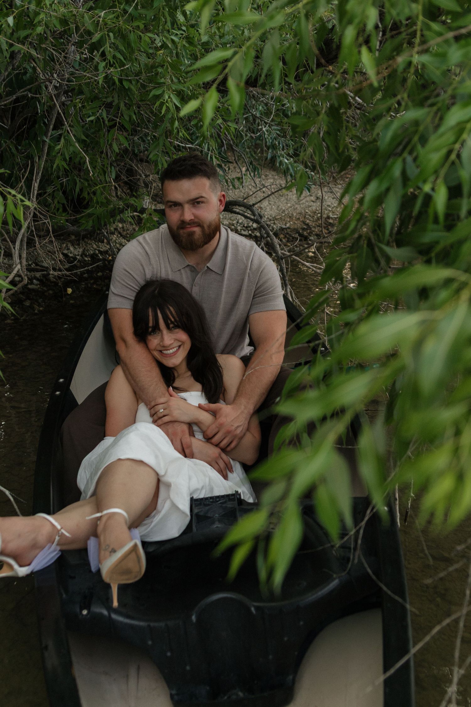 A romantic moment captured in a canoe under leafy branches near the shoreline.