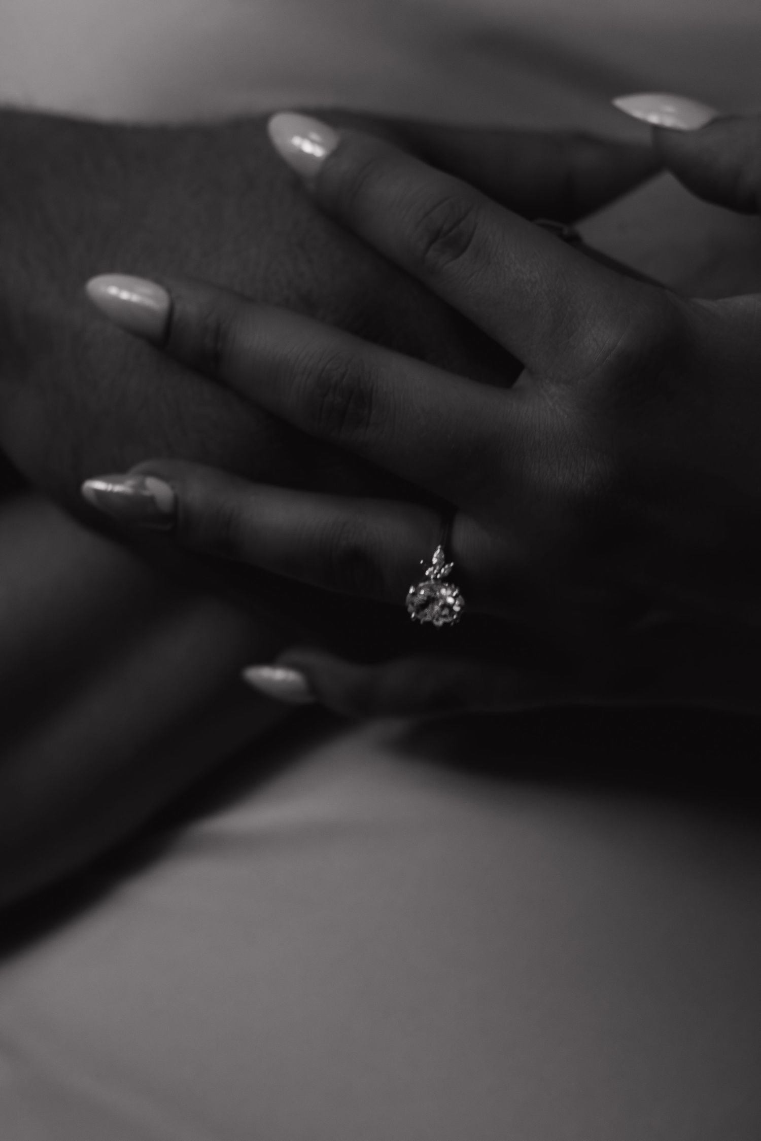 Close-up black and white photograph of hands with a sparkling diamond ring.