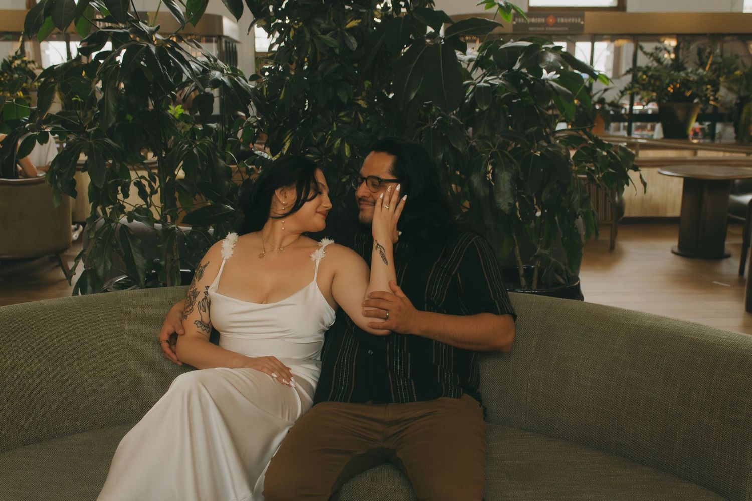 A couple sharing a tender moment among green foliage with one person wearing a white top.