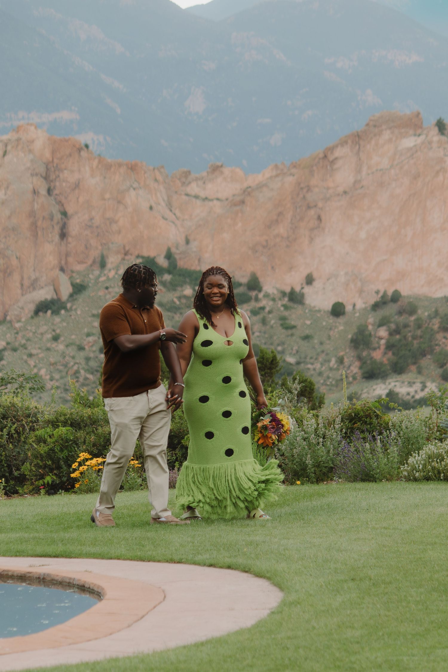 A couple walks near a curved pool with the majestic Garden of the Gods rock formations in view.