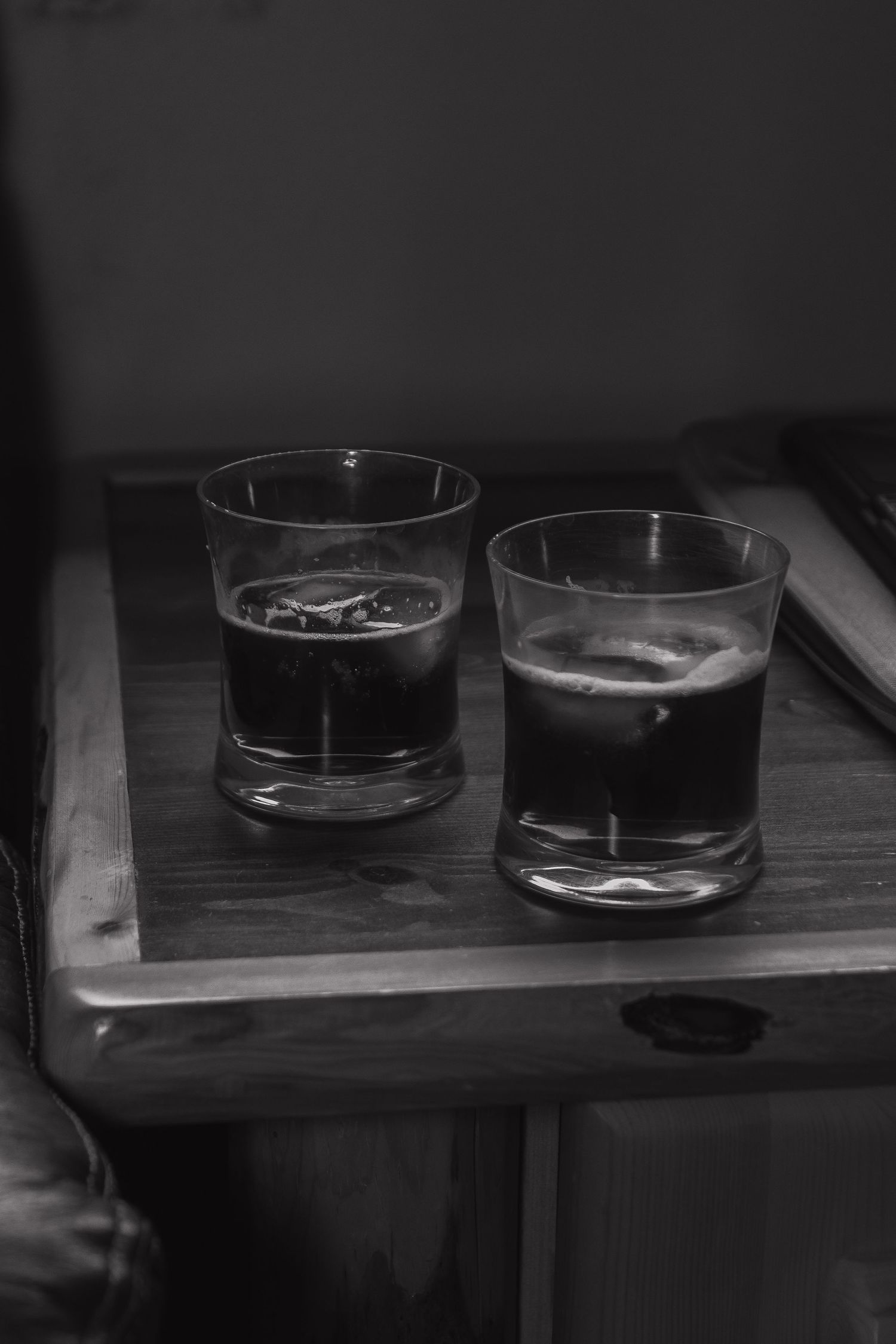 Dark glasses sit on a wooden surface in moody black and white lighting.