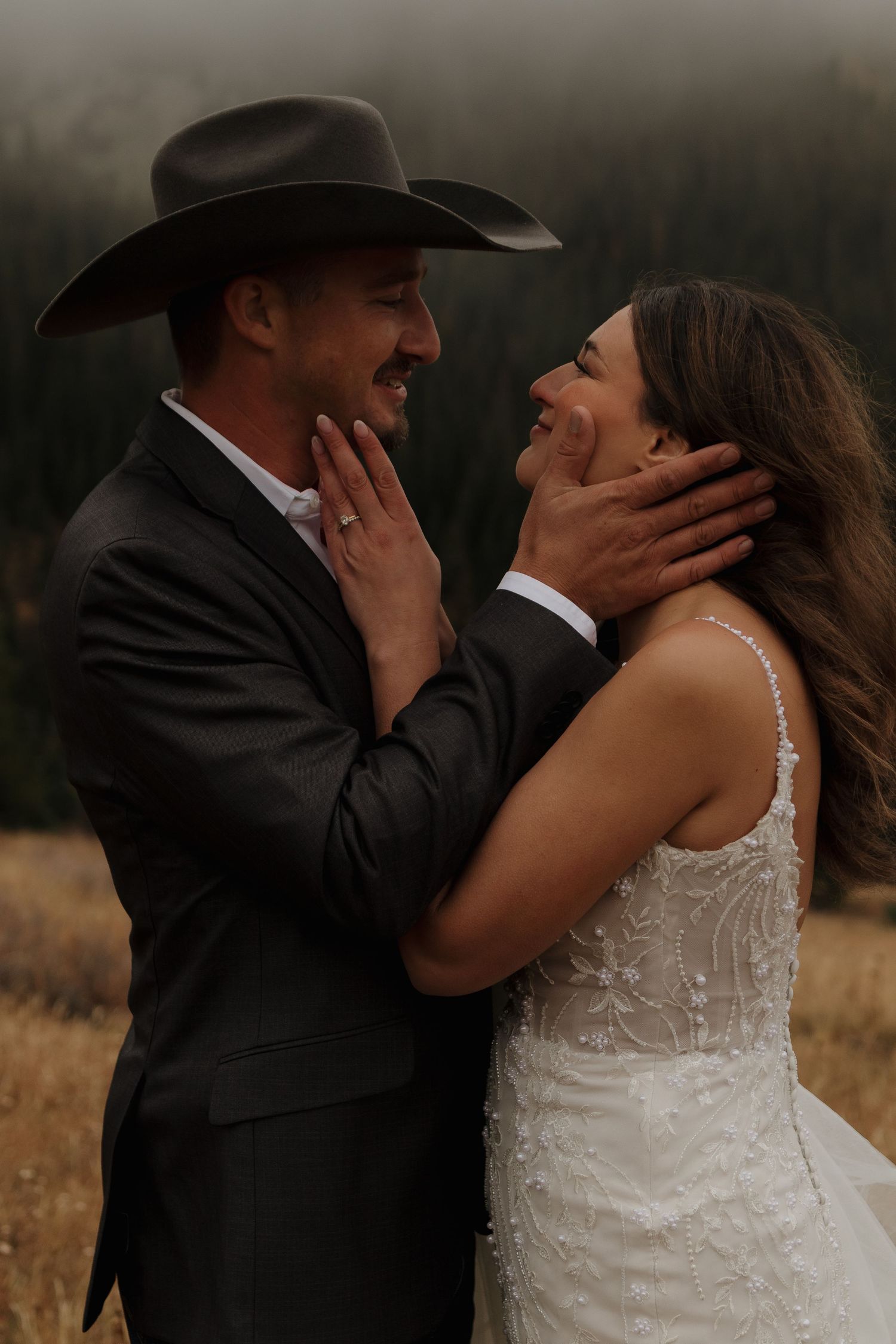 An intimate moment captured between a couple in western attire against a moody outdoor backdrop.