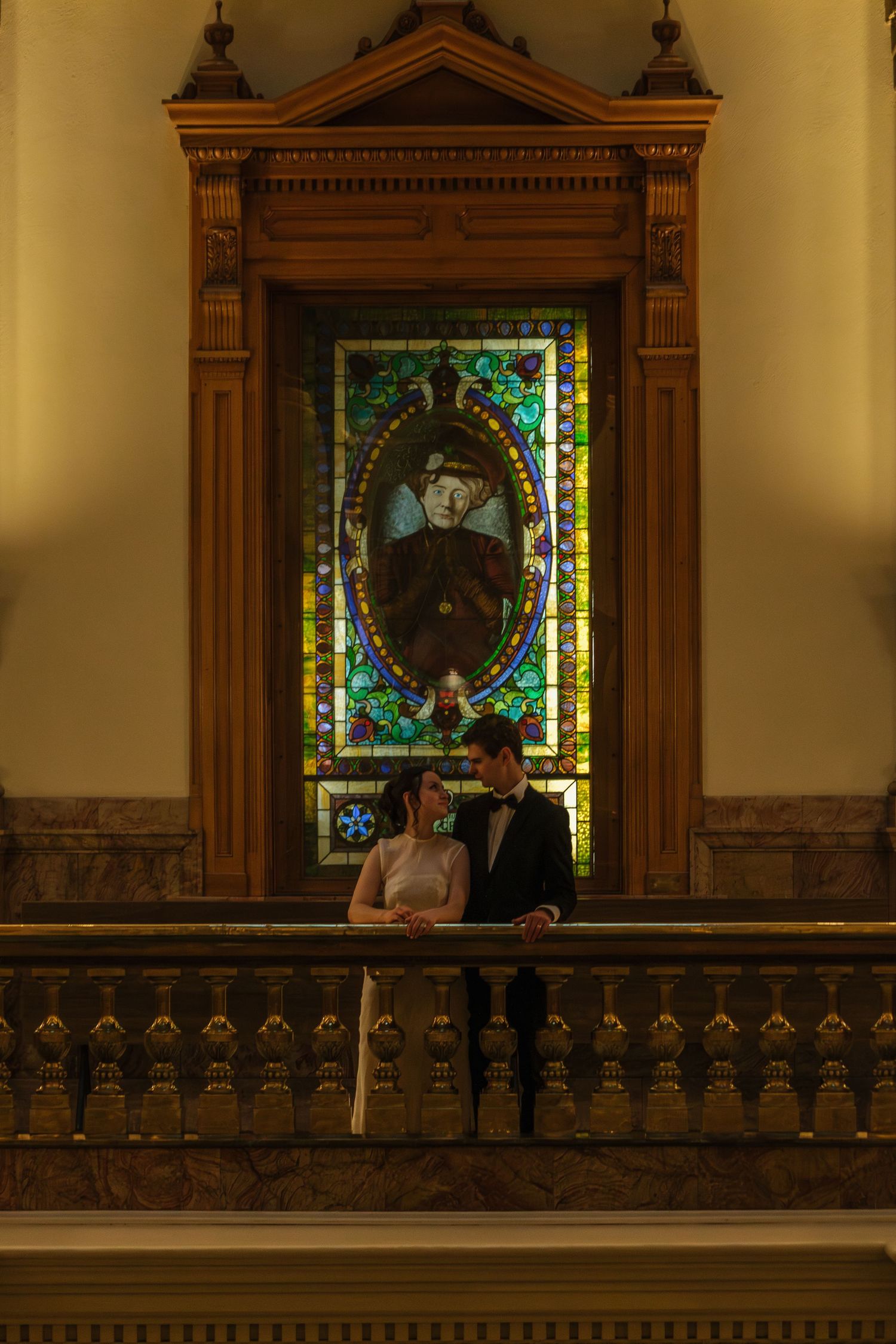 Wedding couple posing in front of stained glass windows in a historic building.