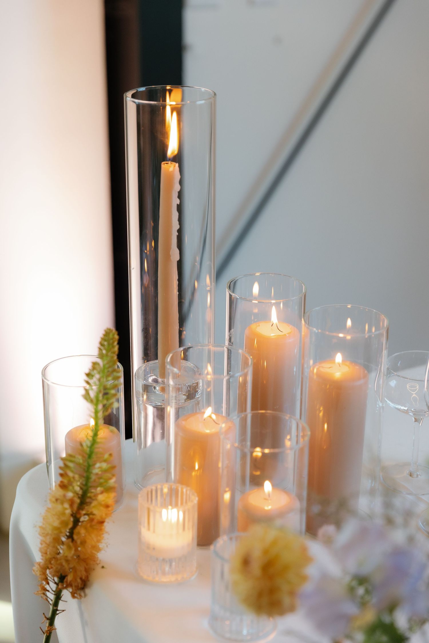 Glass hurricane candle holders with glowing votives and dried flowers create an elegant table centerpiece.