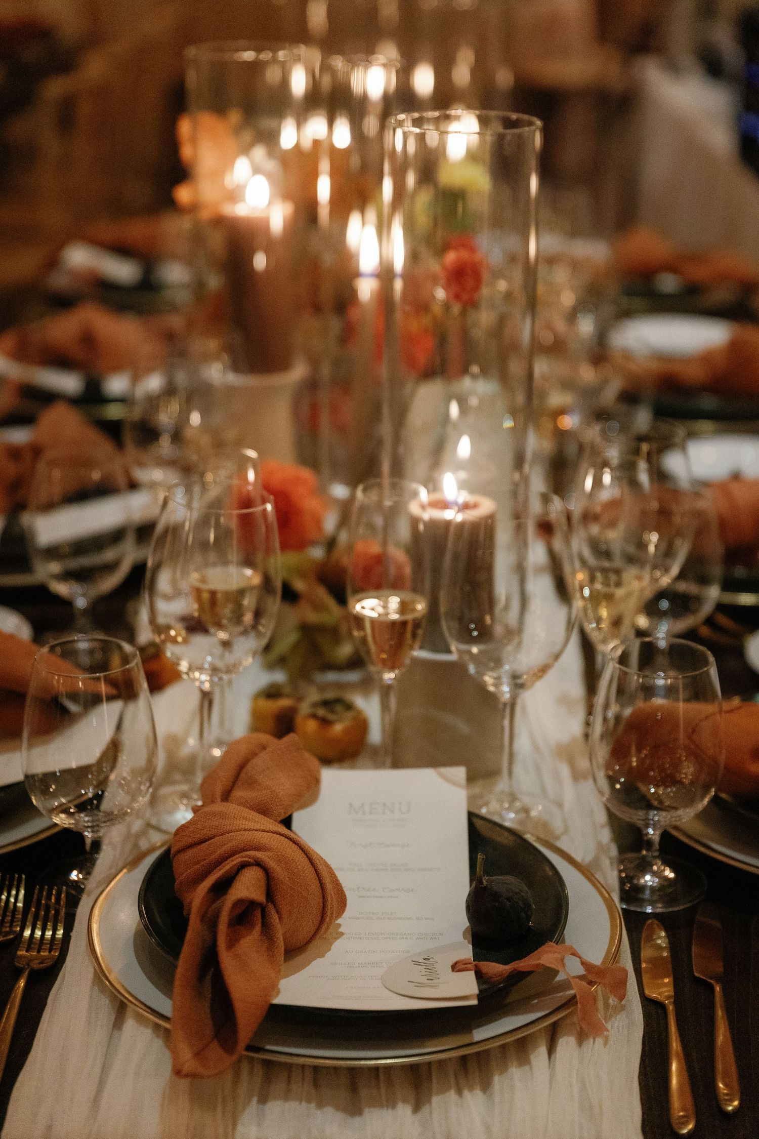 Elegant table settings with brown napkins, wine glasses, and glowing candlelight create an intimate dining atmosphere.