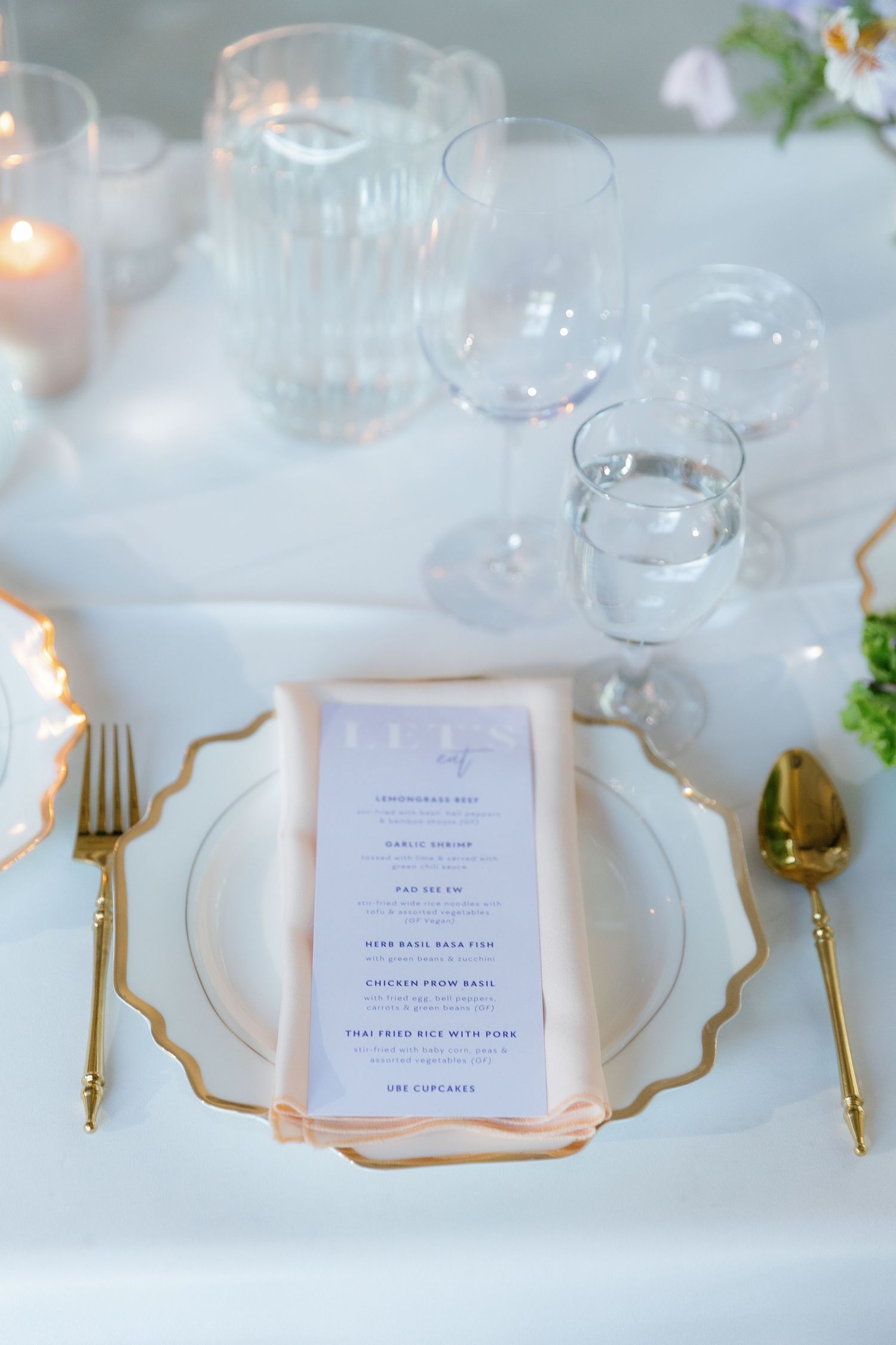 Elegant table setting with gold cutlery, crystal glasses and menu cards on white linens.