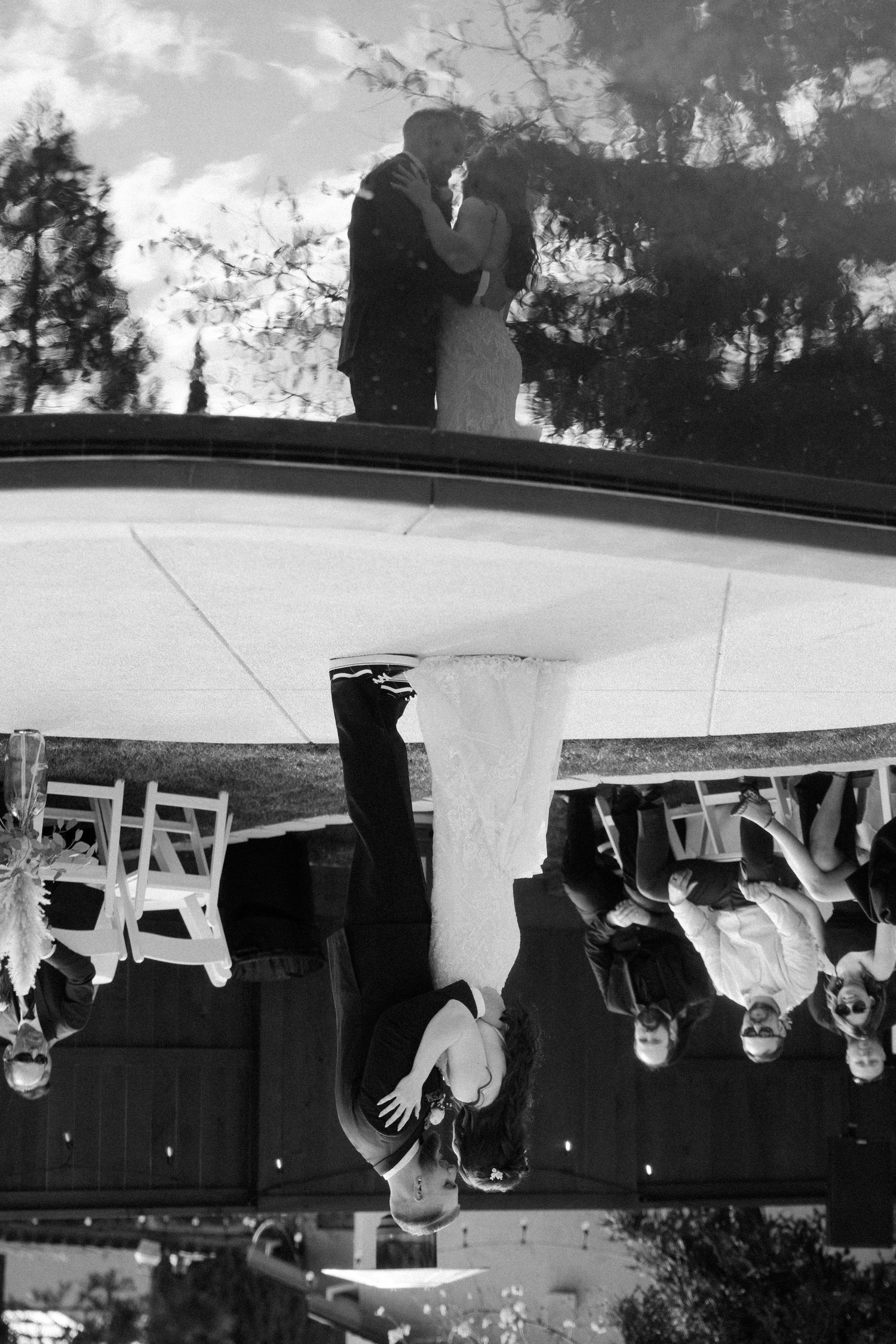 Black and white wedding photo showing silhouettes of a couple on top with reception guests visible below through a tent canopy.
