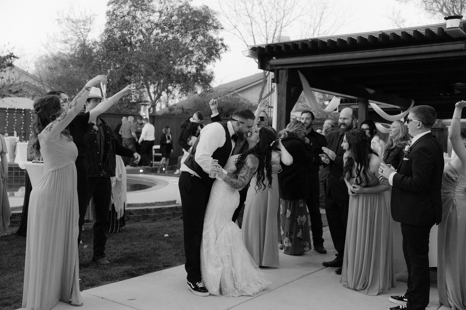 Wedding party members in formal attire pose for photos outdoors during a celebration.