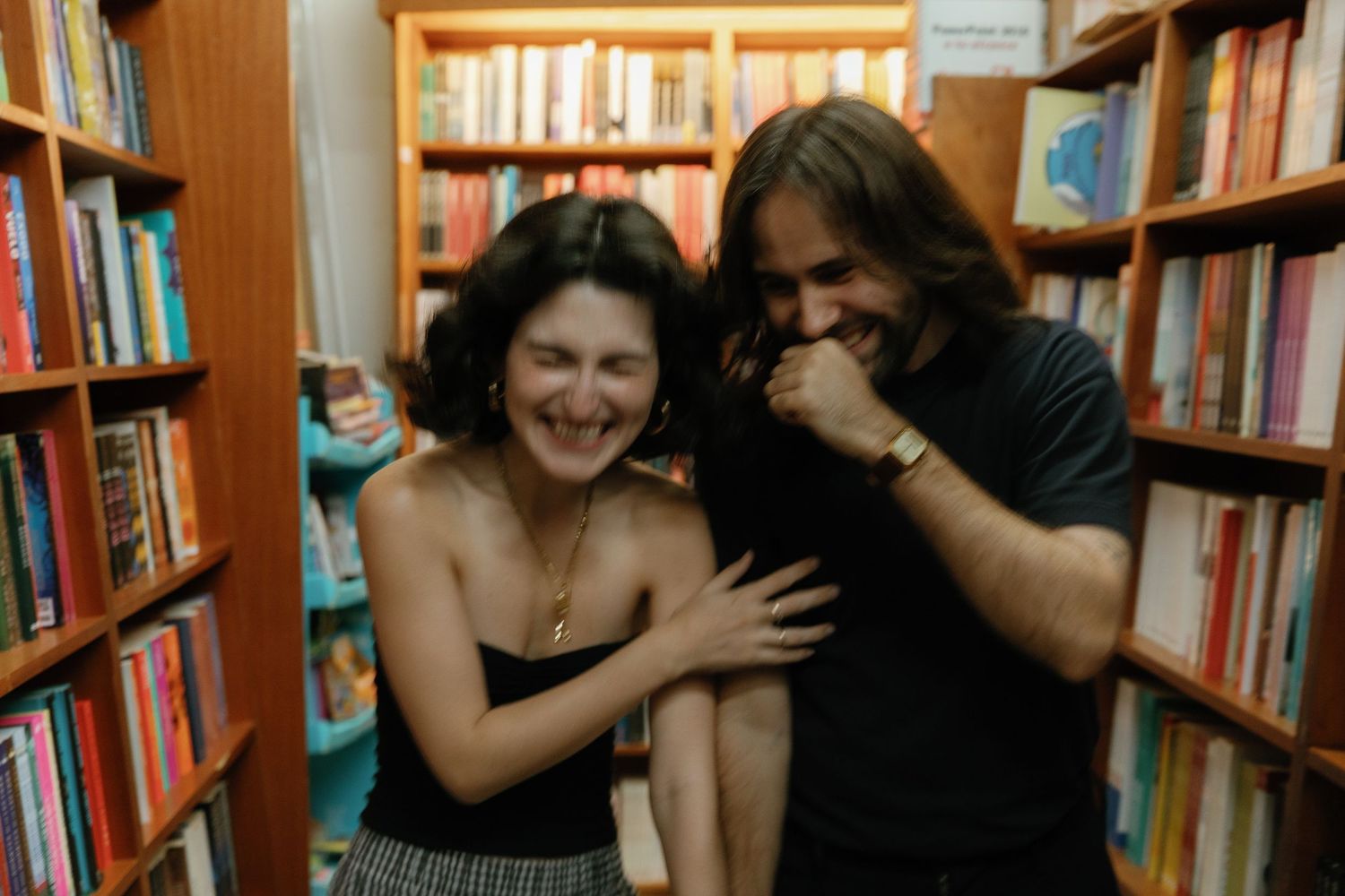 Two people playfully interact between library bookshelves in a sequence of candid moments.