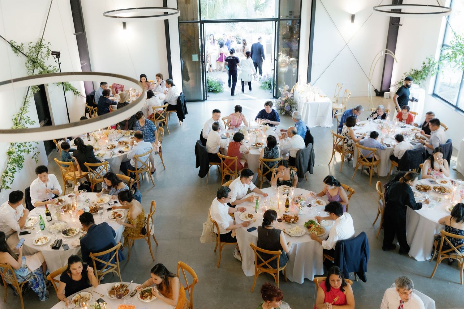 Overhead view of a modern wedding reception with round tables and guests dining in a bright, airy venue.