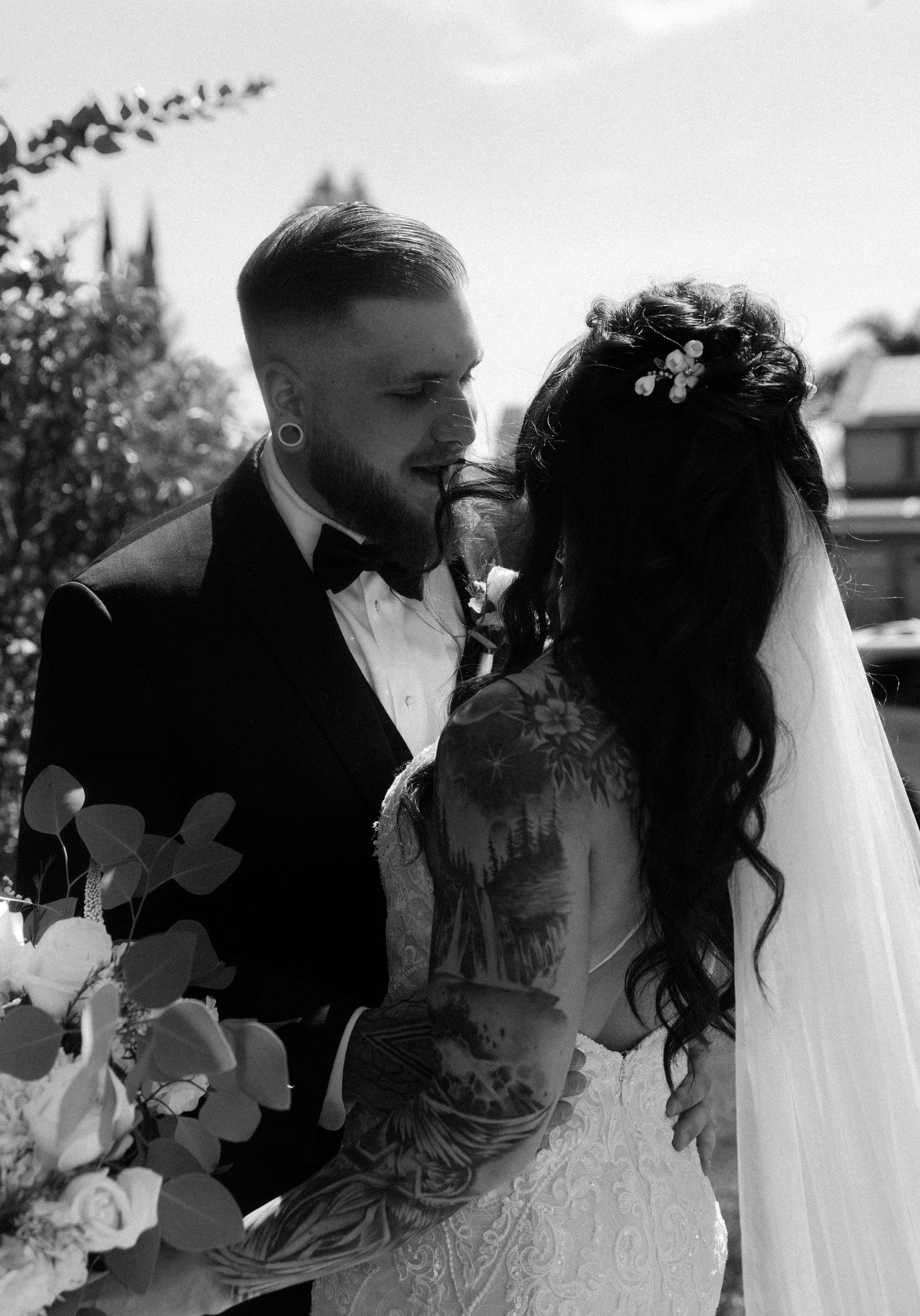 Black and white photo of newlyweds sharing an intimate moment outdoors during their wedding ceremony.