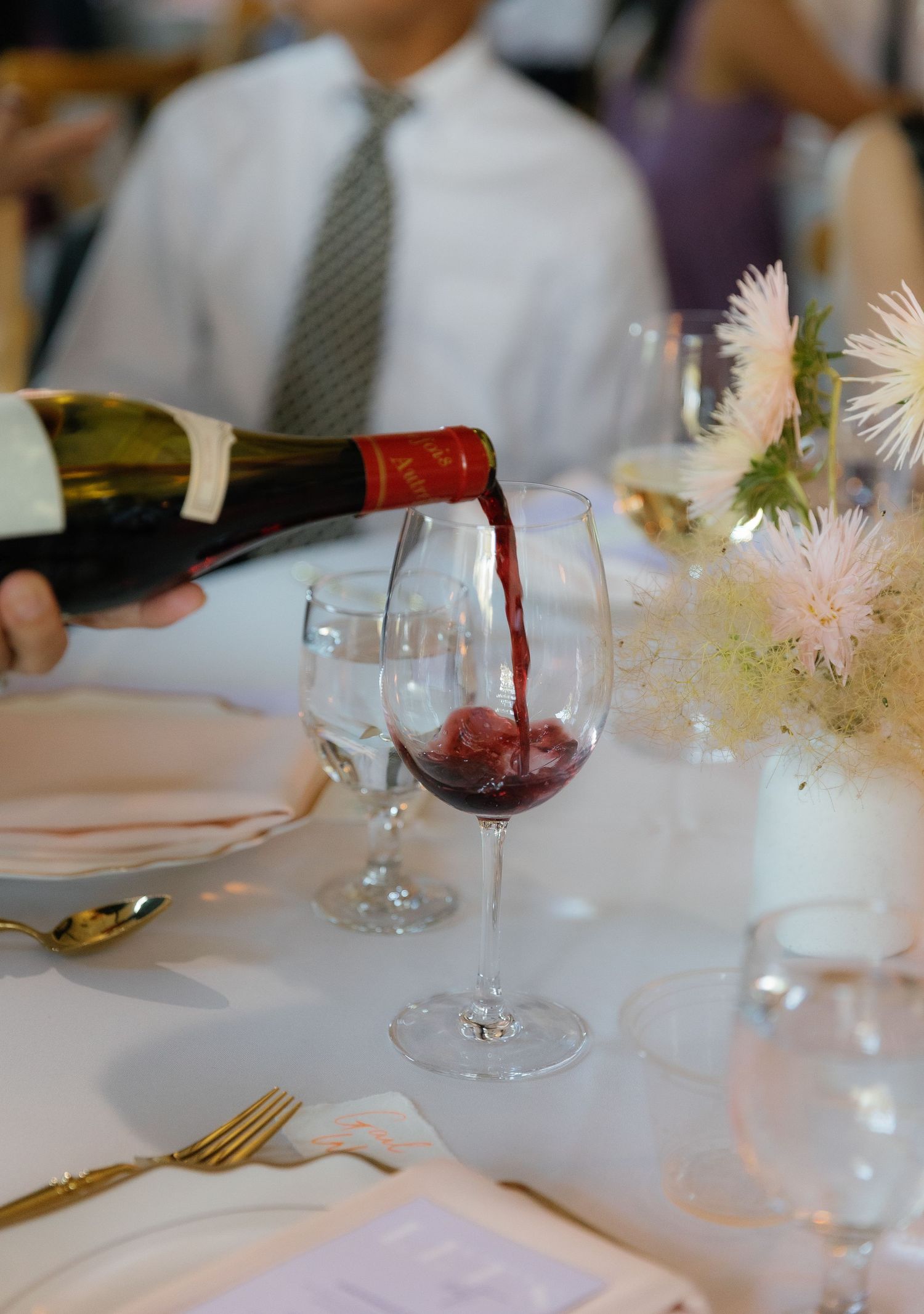 Red wine being poured into crystal glasses at an elegant dinner table setting.