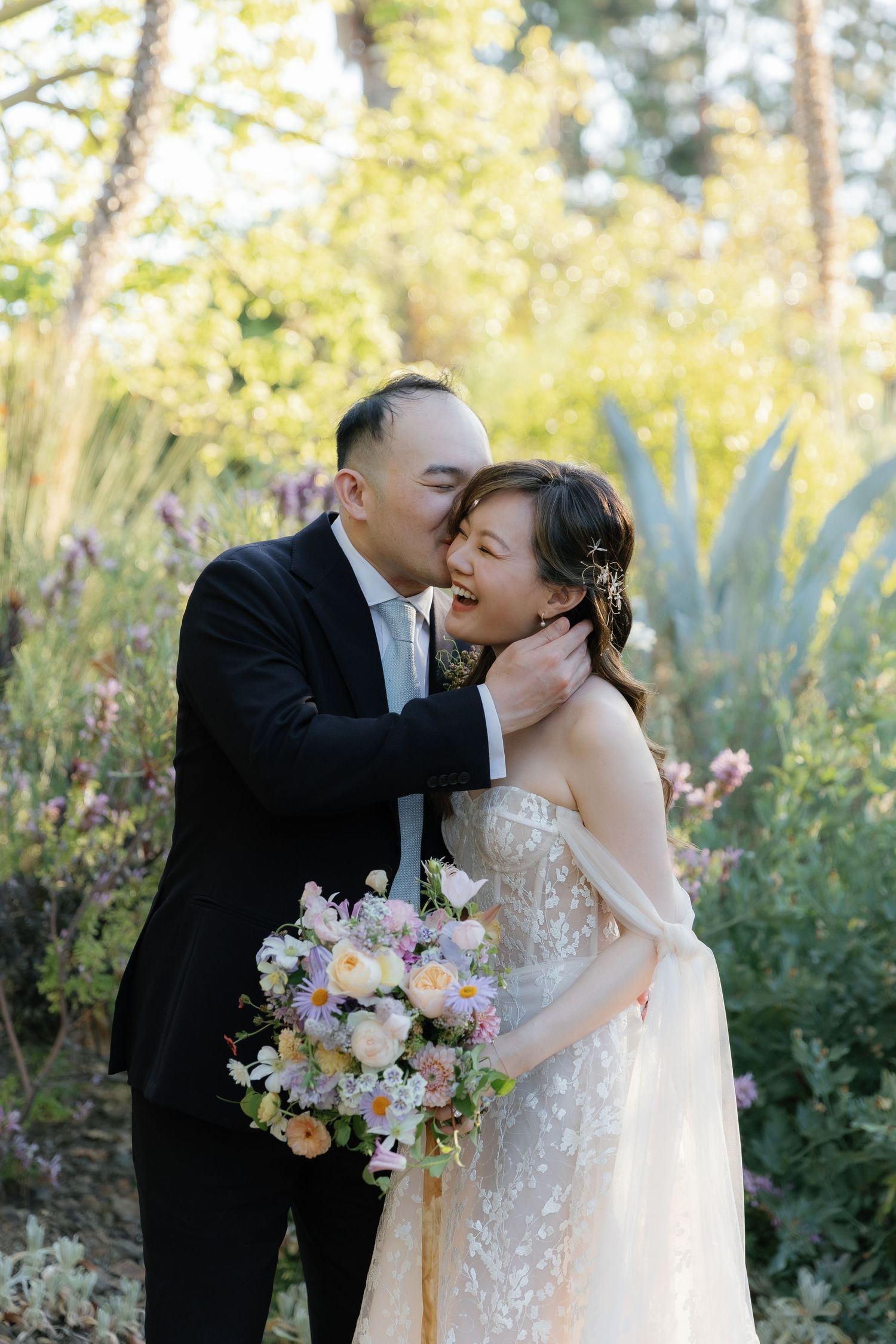 A tender moment shared between newlyweds in a garden setting with a pastel bouquet.