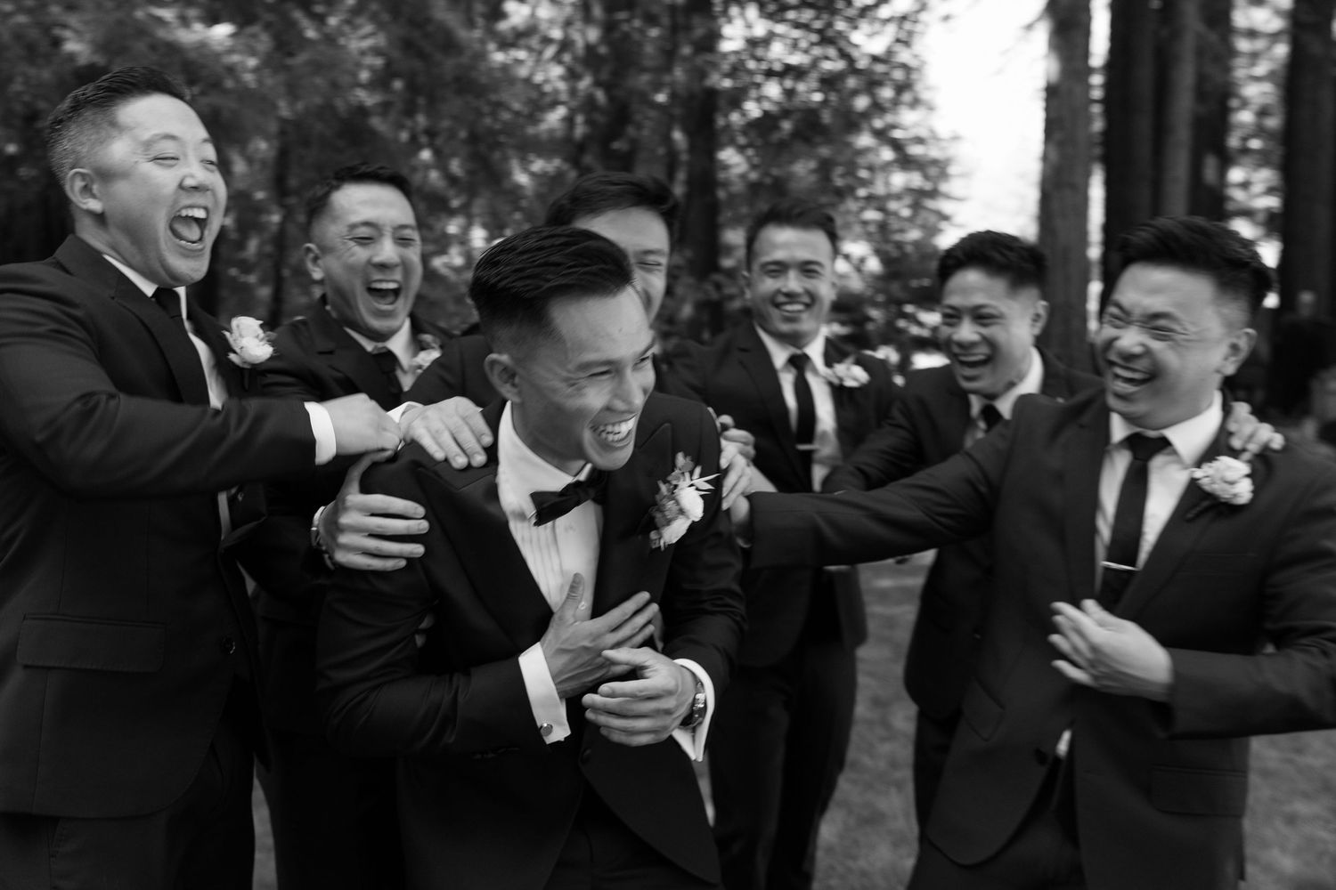 Groomsmen laughing and embracing in a candid black and white photo during wedding celebrations.