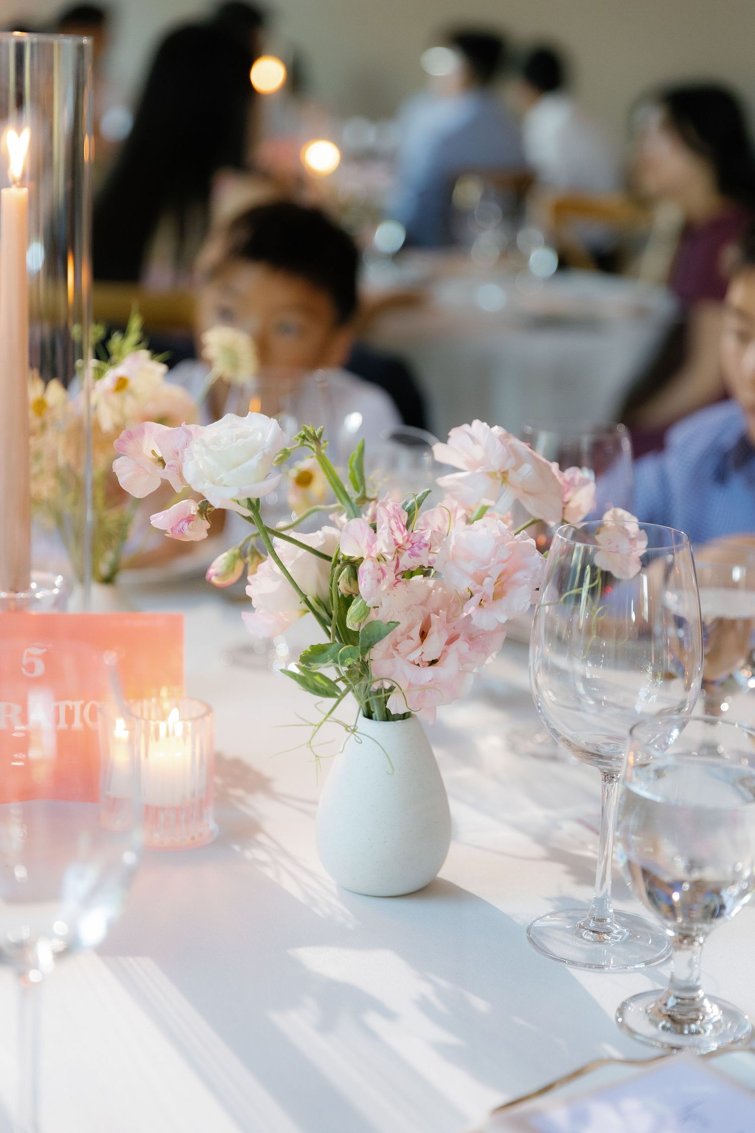 Romantic wedding reception table with soft pink flowers in white vases and glowing candlelight.