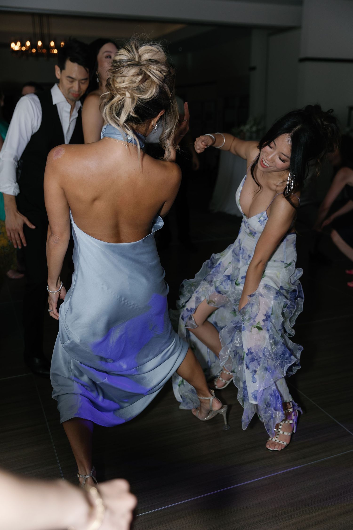 Wedding guests dancing energetically on a dark dance floor with blue lighting effects.