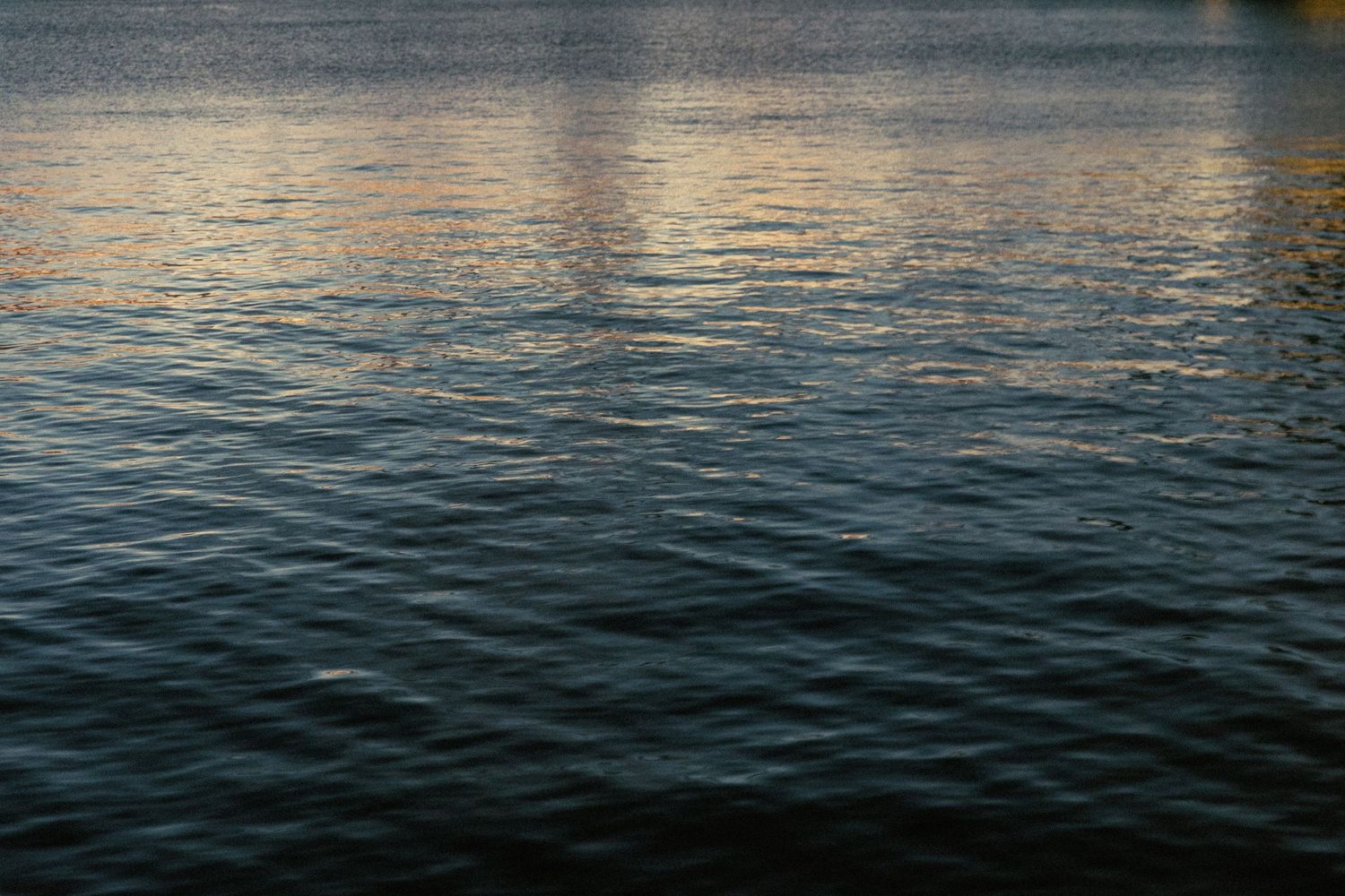 Tranquil dark blue ocean water ripples reflecting sunlight at dusk creating a peaceful seascape pattern.