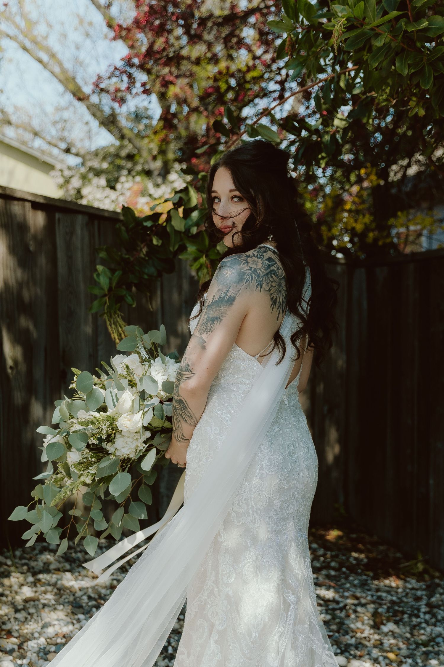 A wedding dress with delicate lace details and a flowing train is showcased in an outdoor garden setting.
