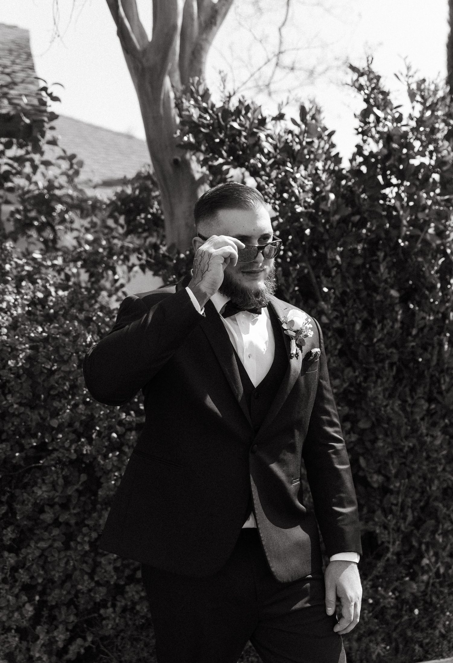 A series of black and white photos showing a man in a suit and tie standing outdoors near foliage.