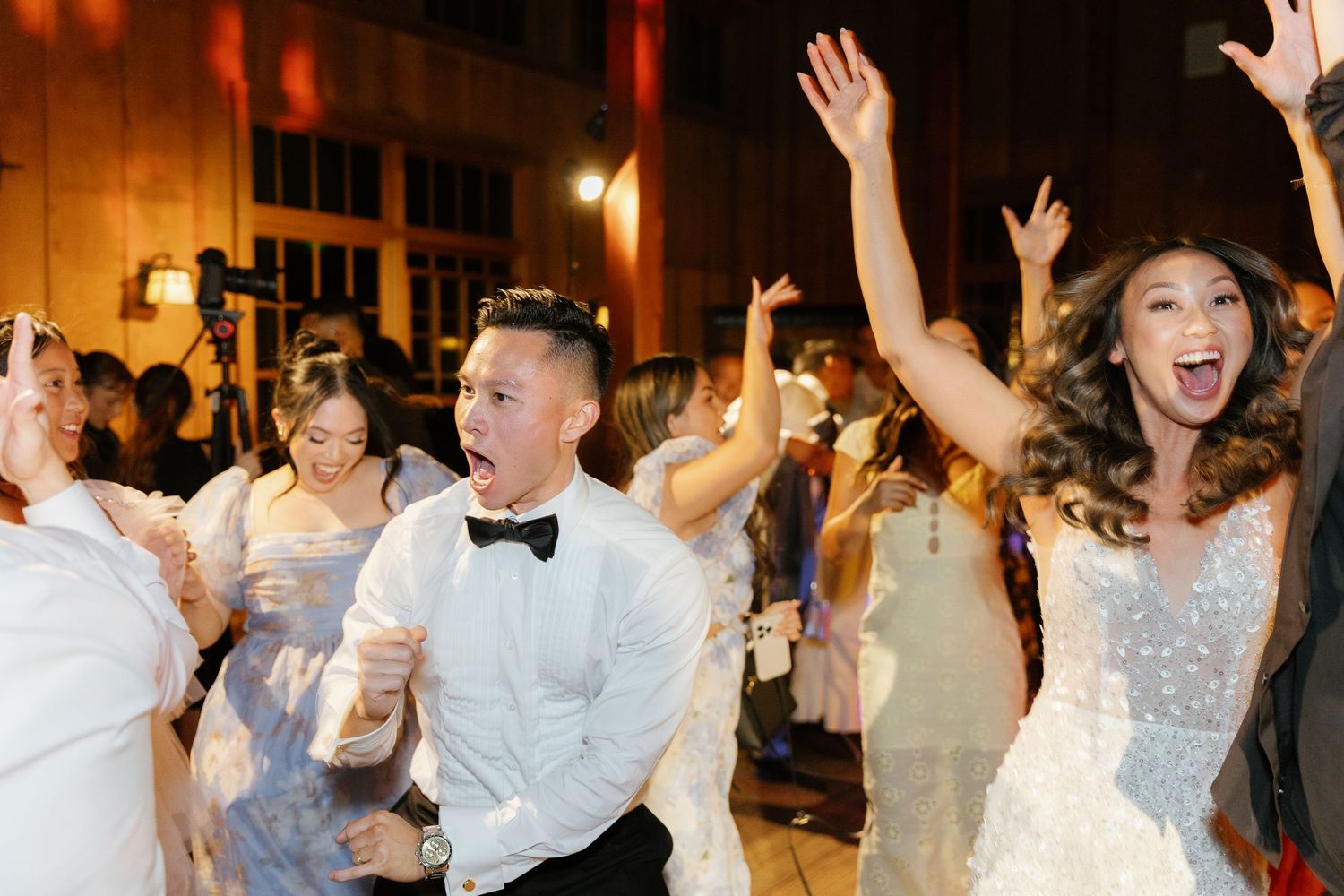 Wedding party dancing and celebrating with raised arms on an illuminated dance floor.