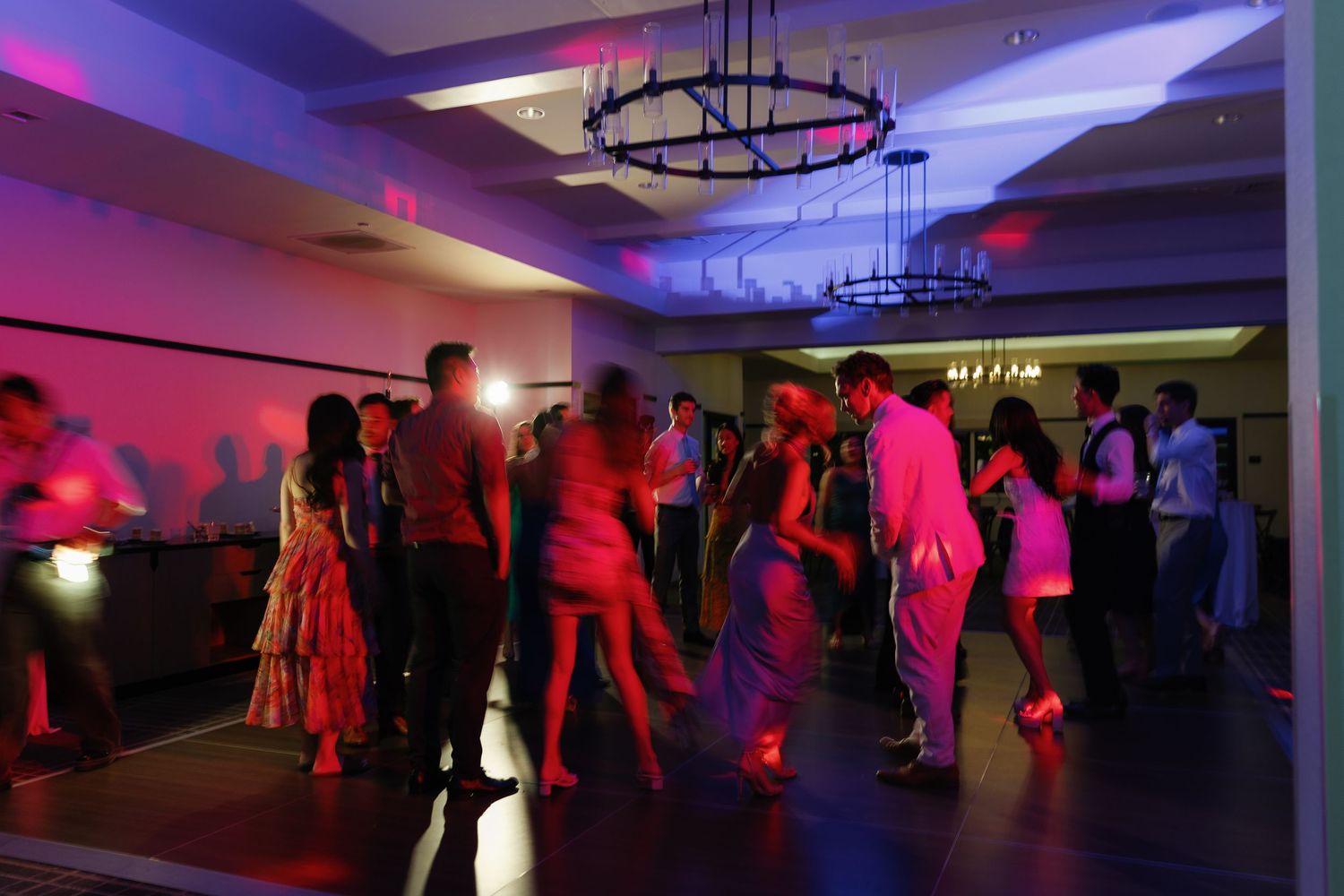 A wedding reception dance floor illuminated with vibrant purple and red lighting creates a party atmosphere.