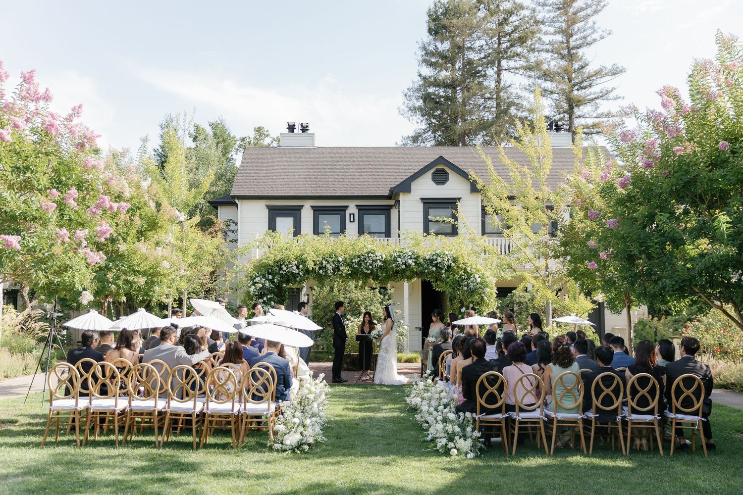 A series of outdoor wedding ceremony photos showing wooden chairs arranged on a lawn with trees and buildings in the background.