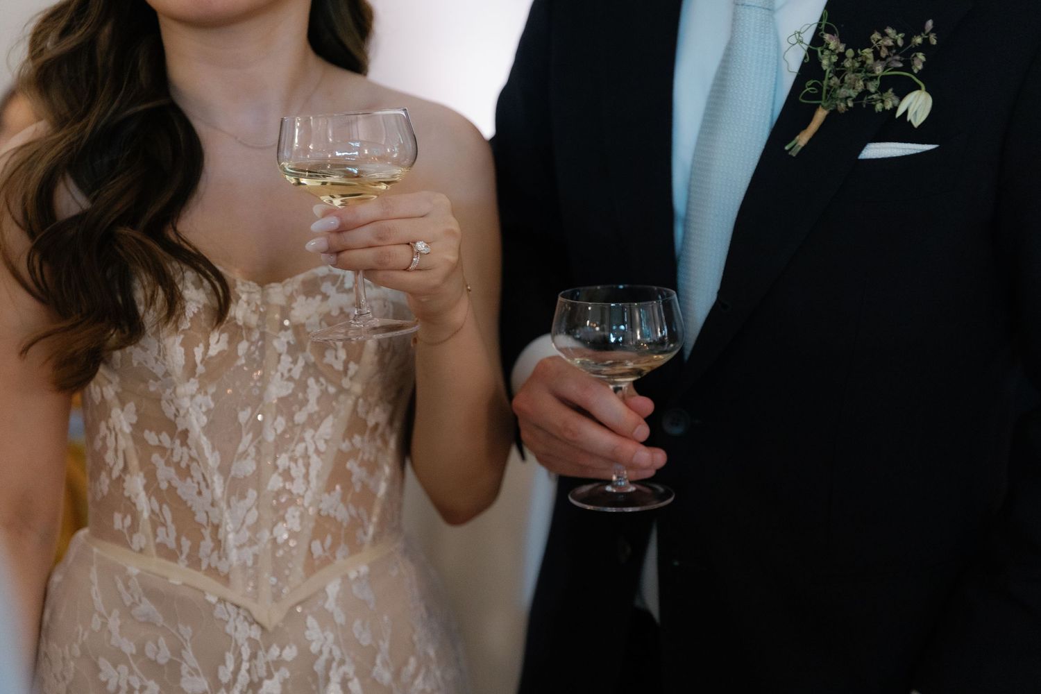 Close-up of champagne glasses held by a couple in formal wedding attire.