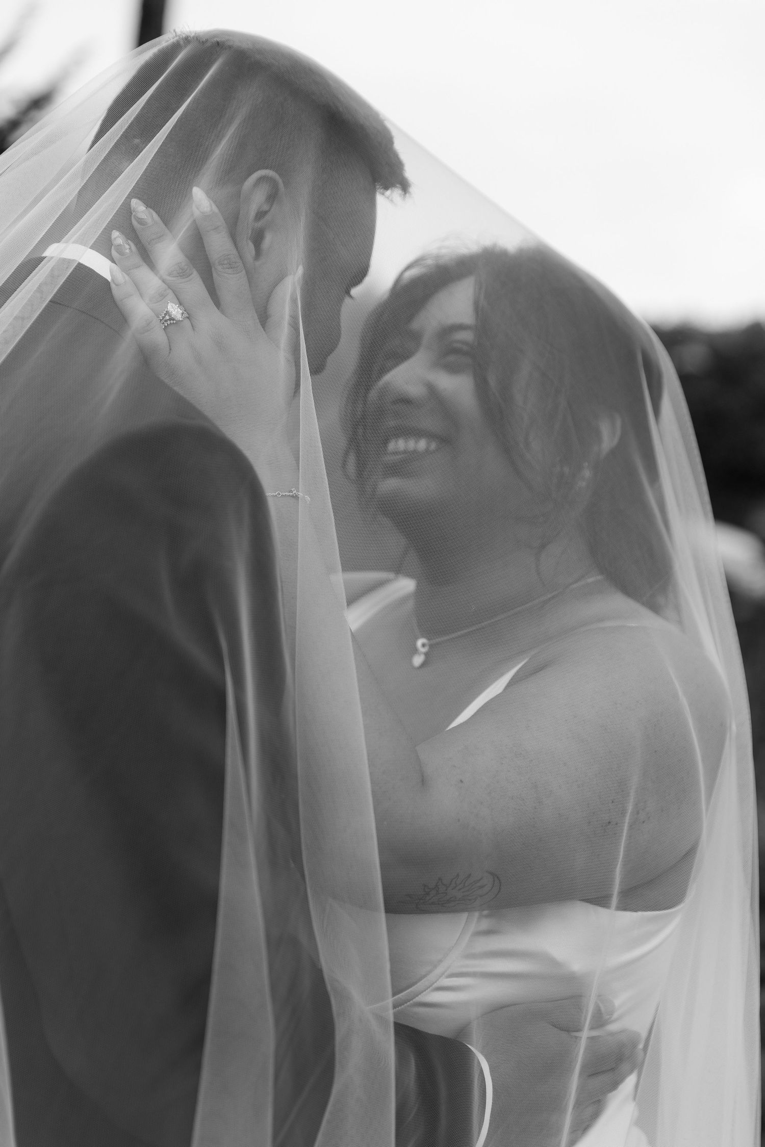 A romantic black and white wedding photo showing a couple sharing an intimate moment under a delicate veil.